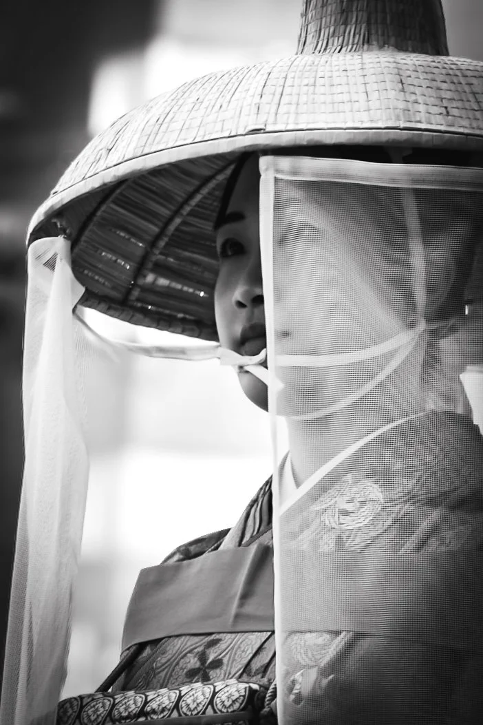 A woman wearing traditional Asian attire and a conical hat with a face shield.
