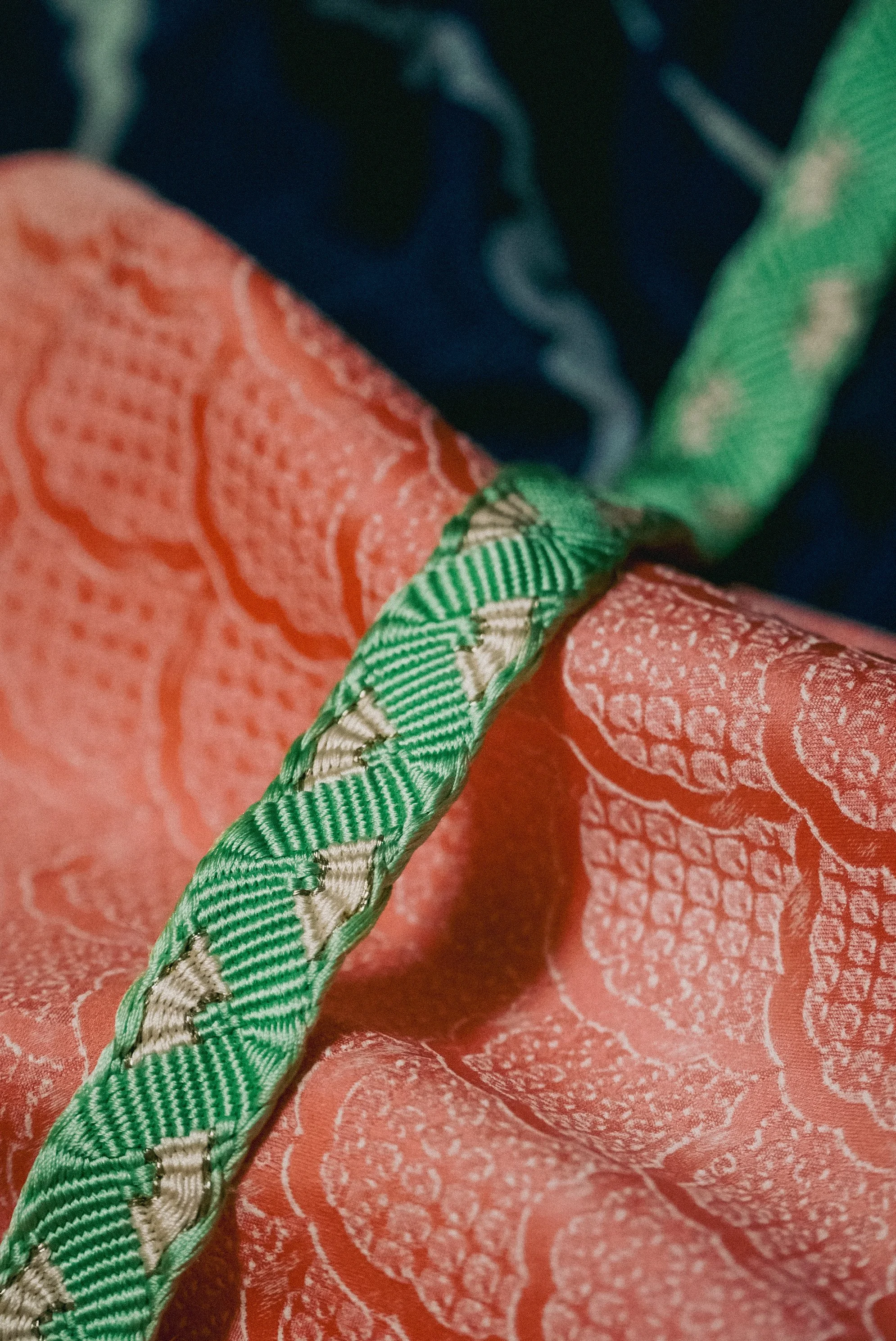 Close-up of a green and beige braided cord resting on a textured orange fabric with a pattern of white floral and leaf designs.