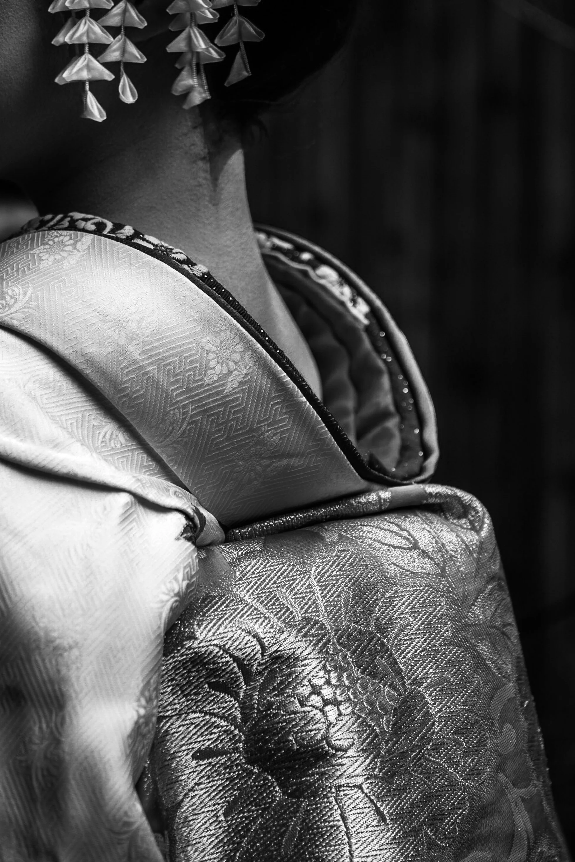Close-up of a person wearing traditional Japanese kimono with detailed fabric patterns and kimono accessories in black and white.