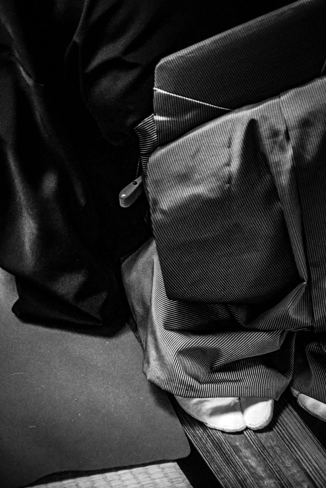 Close-up of a backpack with striped pattern on a textured surface, next to a black bag and a dark fabric item.