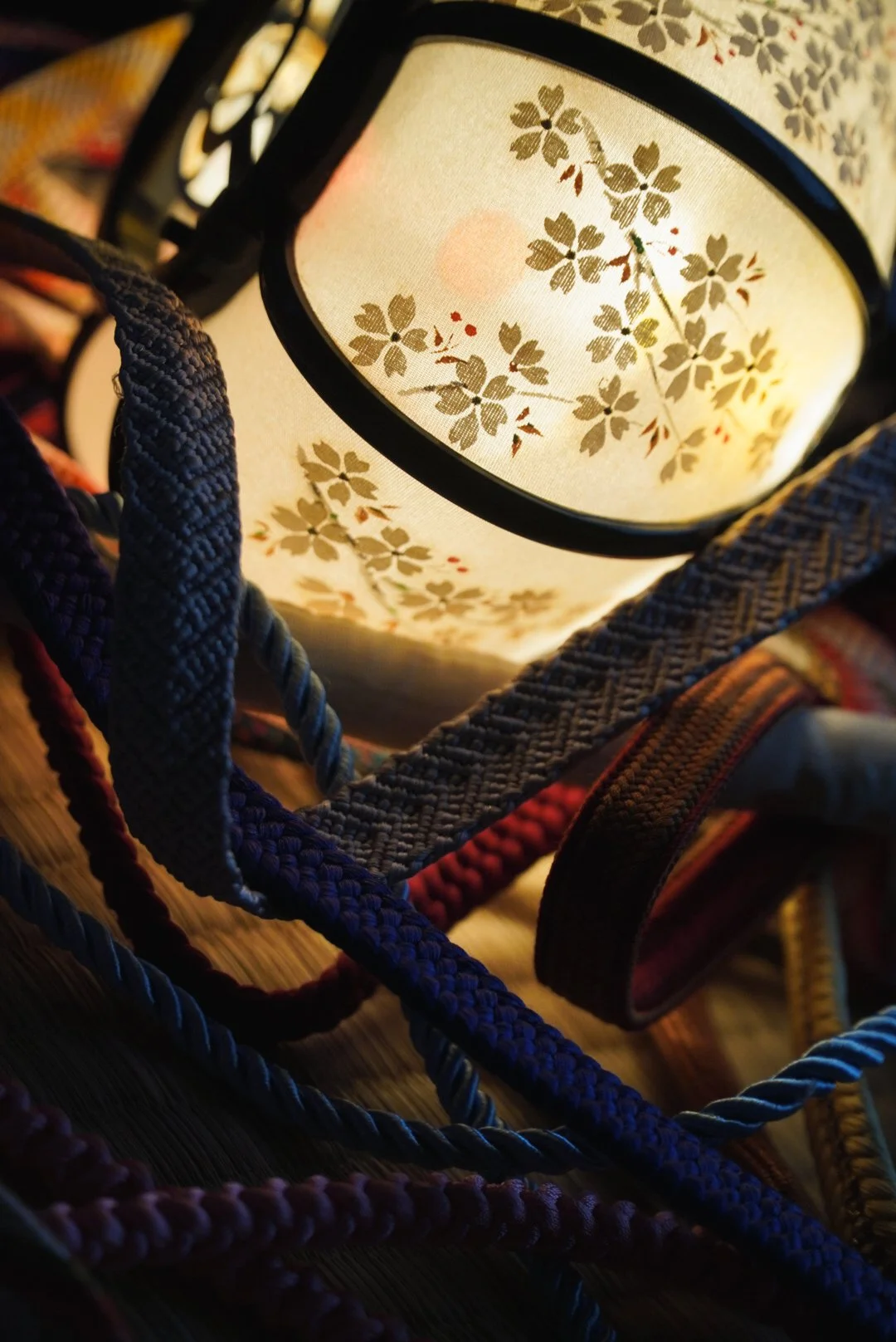 Close-up of a traditional Japanese paper lantern with a floral pattern, surrounded by woven fabric straps and ribbons.