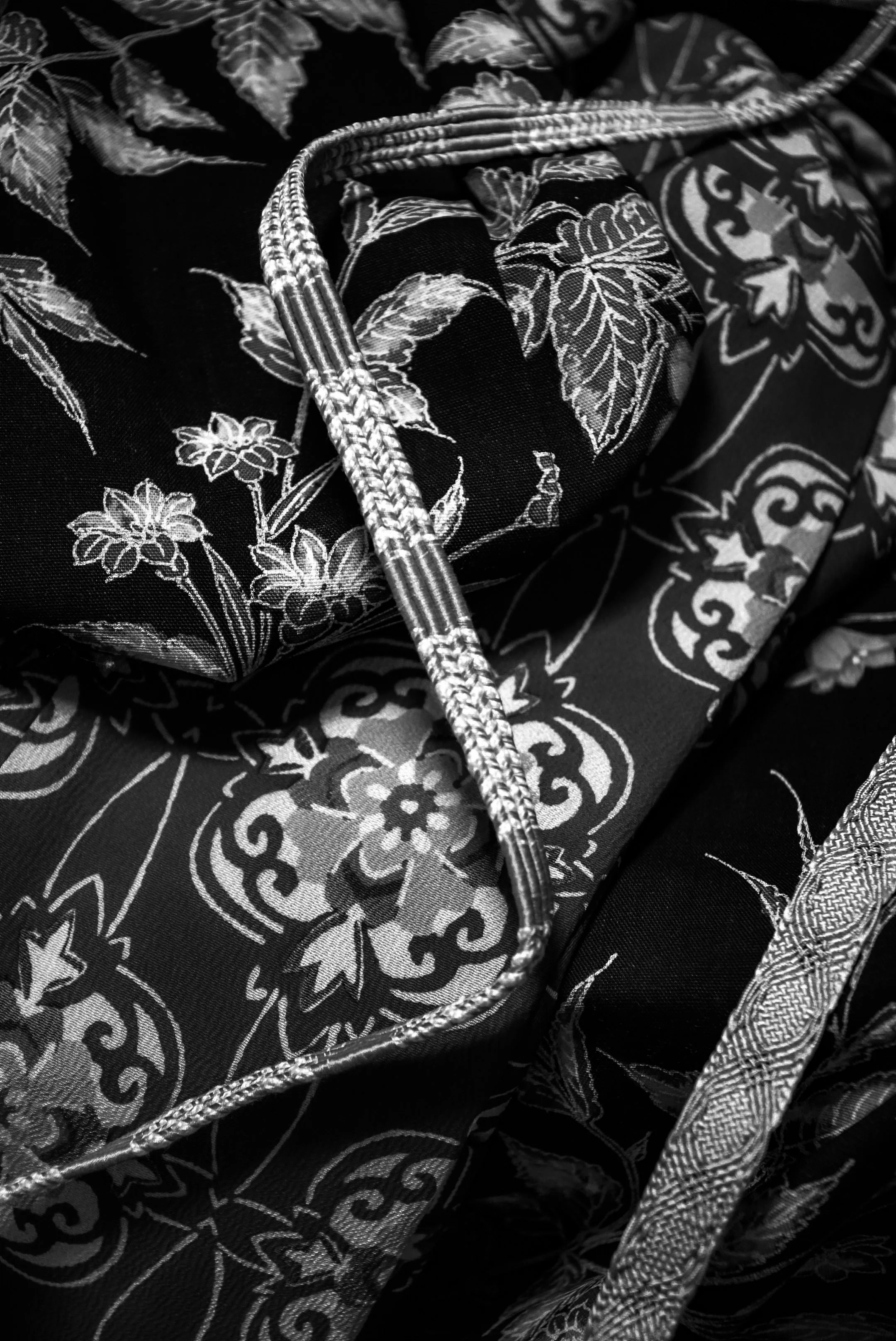 Close-up of a necklace lying on patterned fabric with floral and geometric designs in black and white.