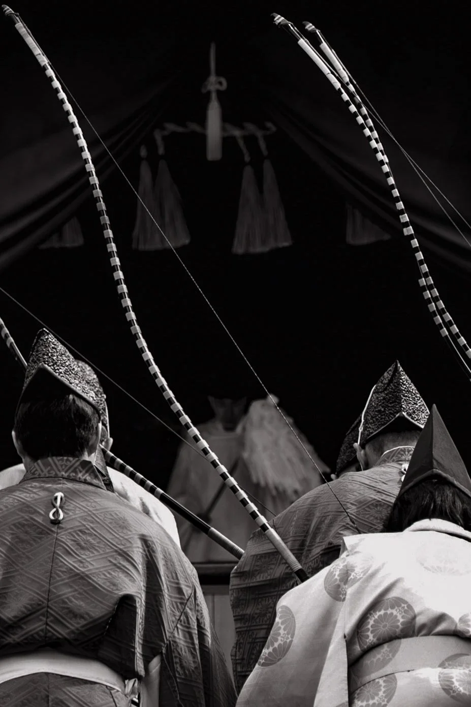 Traditional Japanese Ceremony with three men wearing kimono and hats, seen from behind, under a decorated umbrella.