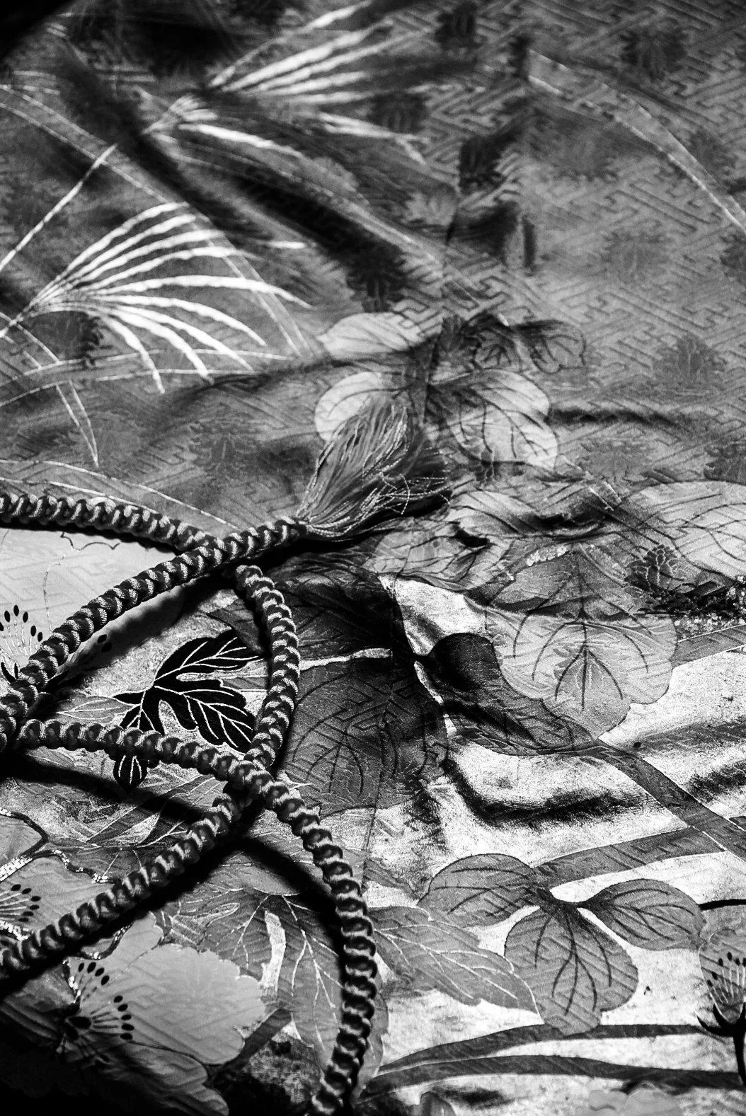 A black and white photo of a gift bag with floral and leaf designs, some flowers appearing to be hibiscus, and a twisted rope handle placed on a patterned surface.