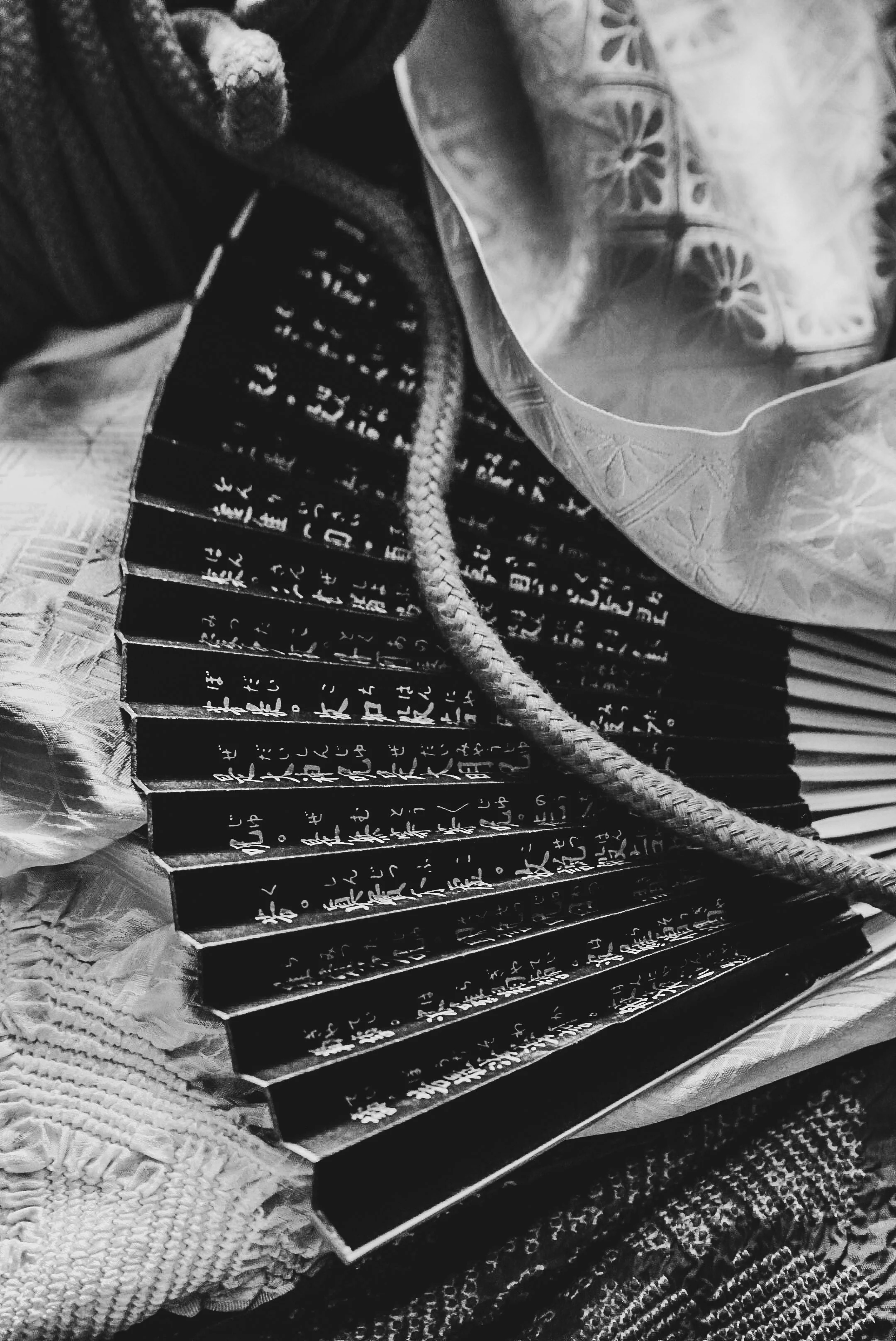 A black and white image showing a close-up of a notebook or journal and other items, with a lace fabric in the background.