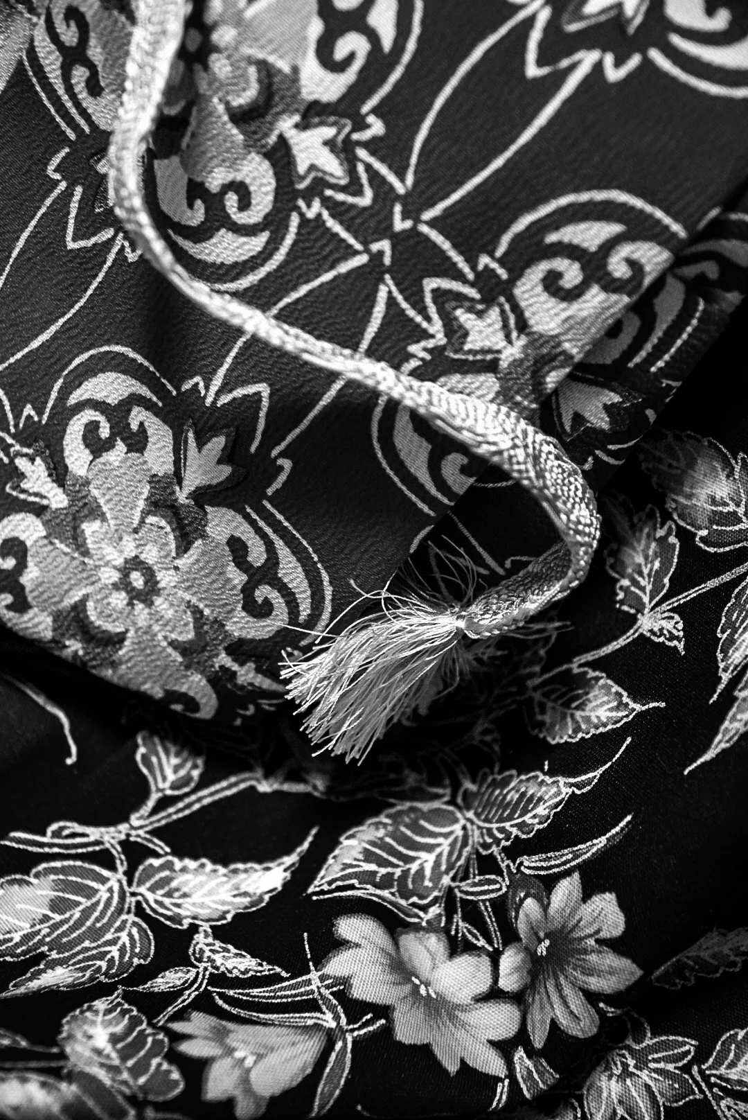 Close-up of a fabric with intricate floral and paisley patterns in black and white, featuring a drawstring with frayed ends.
