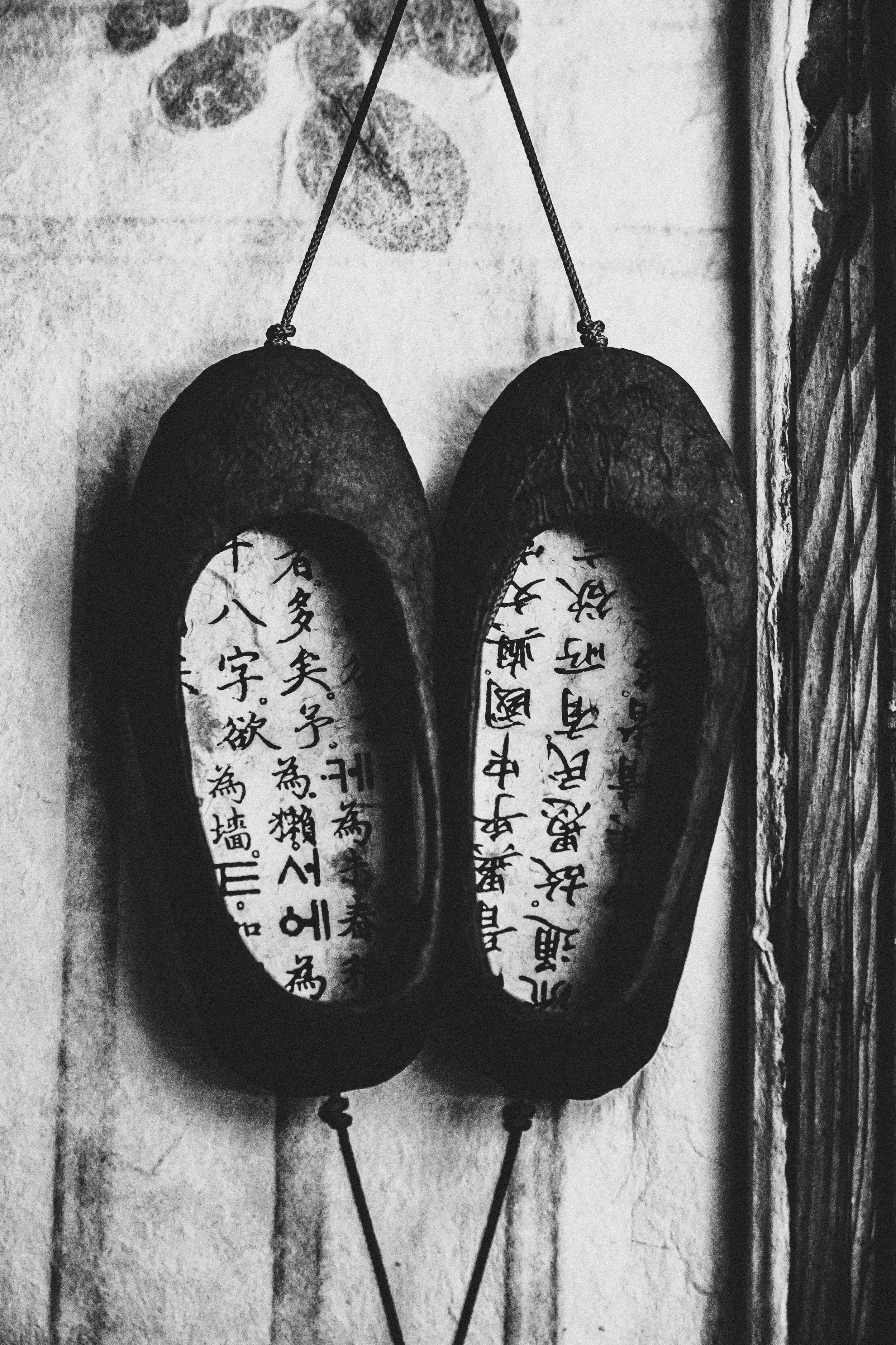 Pair of traditional Japanese wooden sandals with handwritten Japanese characters inside the soles, hung on a wall with ropes.