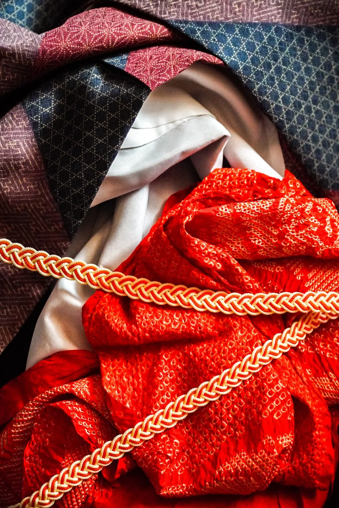 Close-up of a bundle of colorful fabrics, including black, red, and white, with intricate patterns and a decorative orange and cream braided trim.