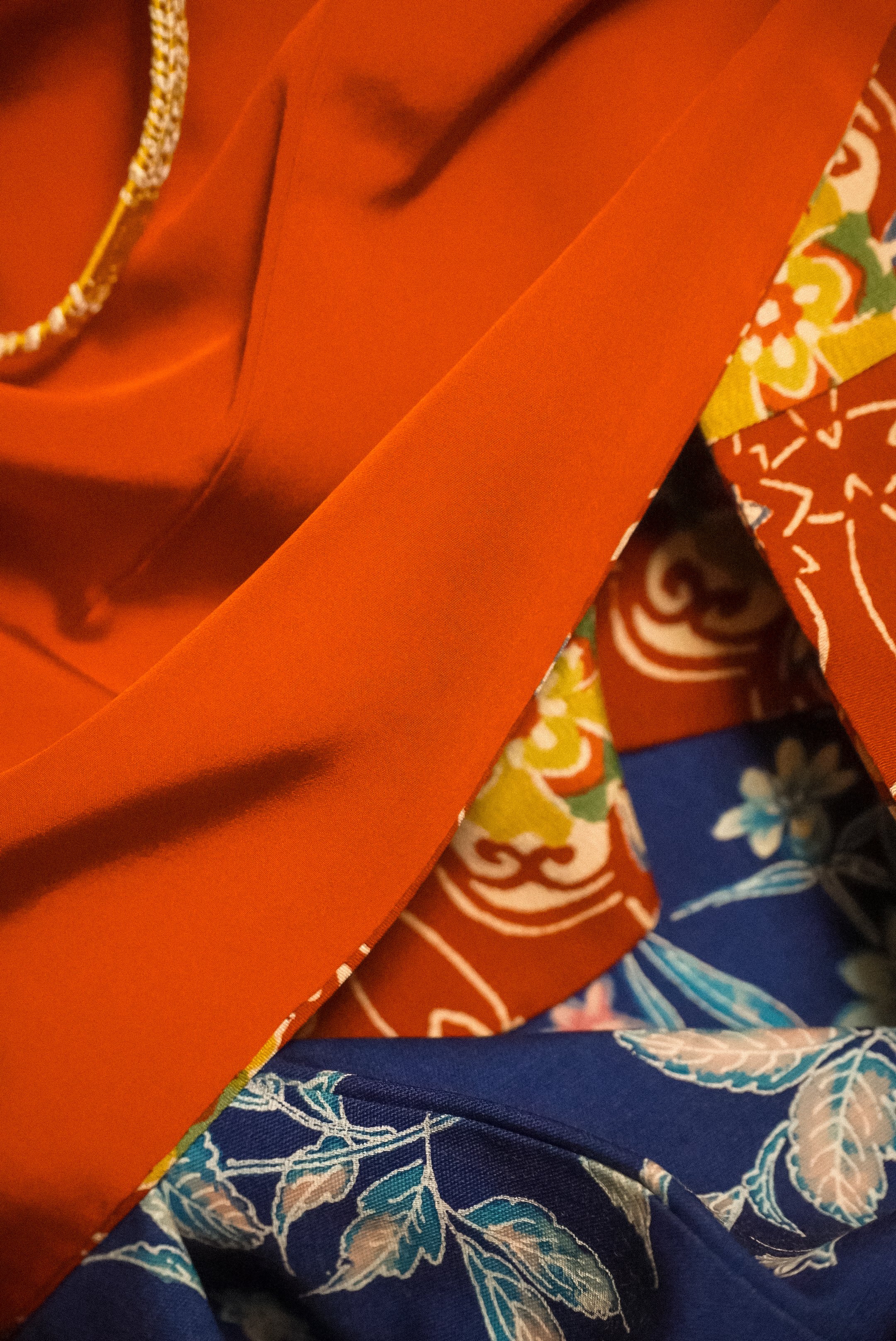 Close-up of layered fabric with bright orange, multicolored floral, and patterned blue and white textiles.