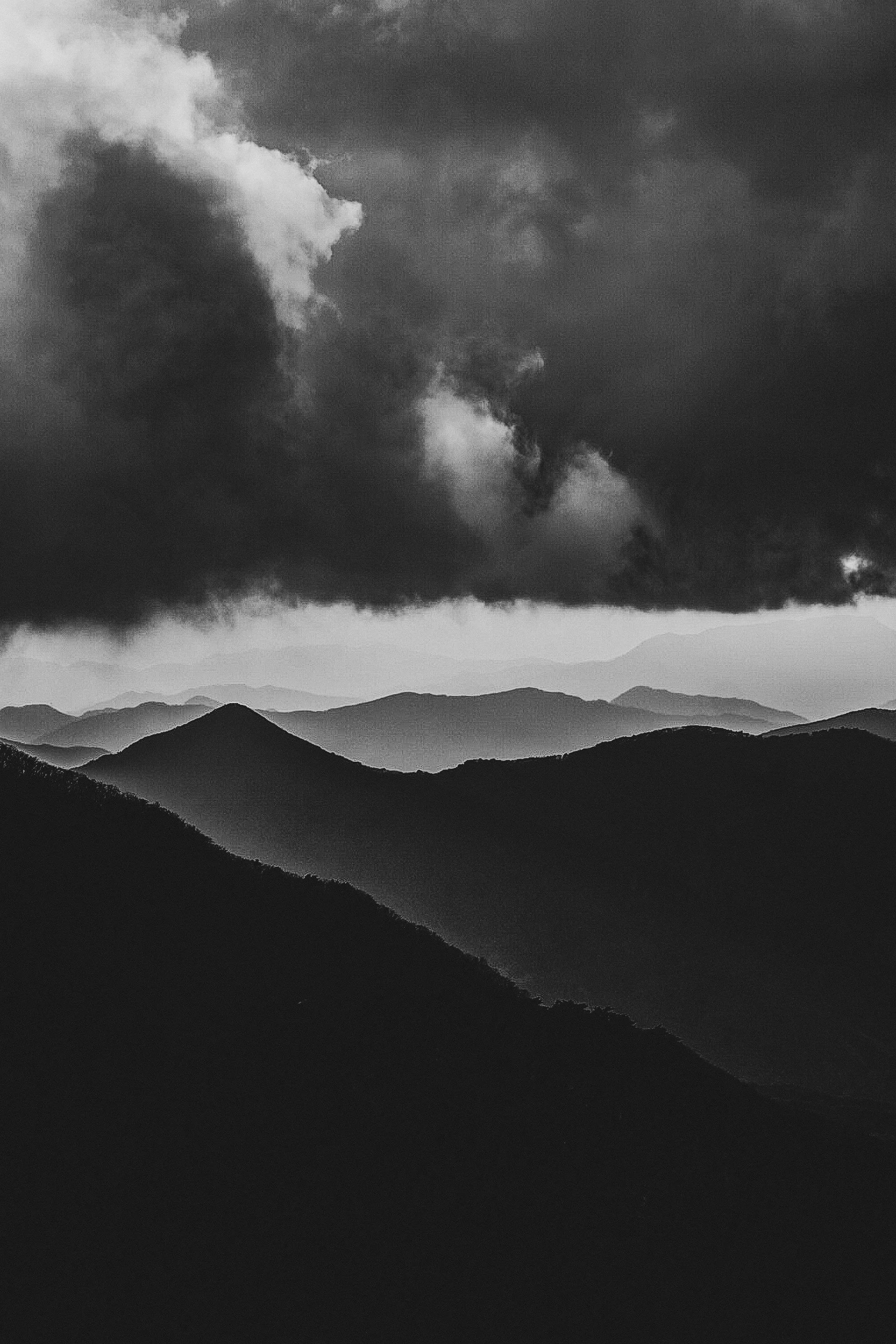 Black and white photograph of mountain ranges under a dark, cloudy sky.