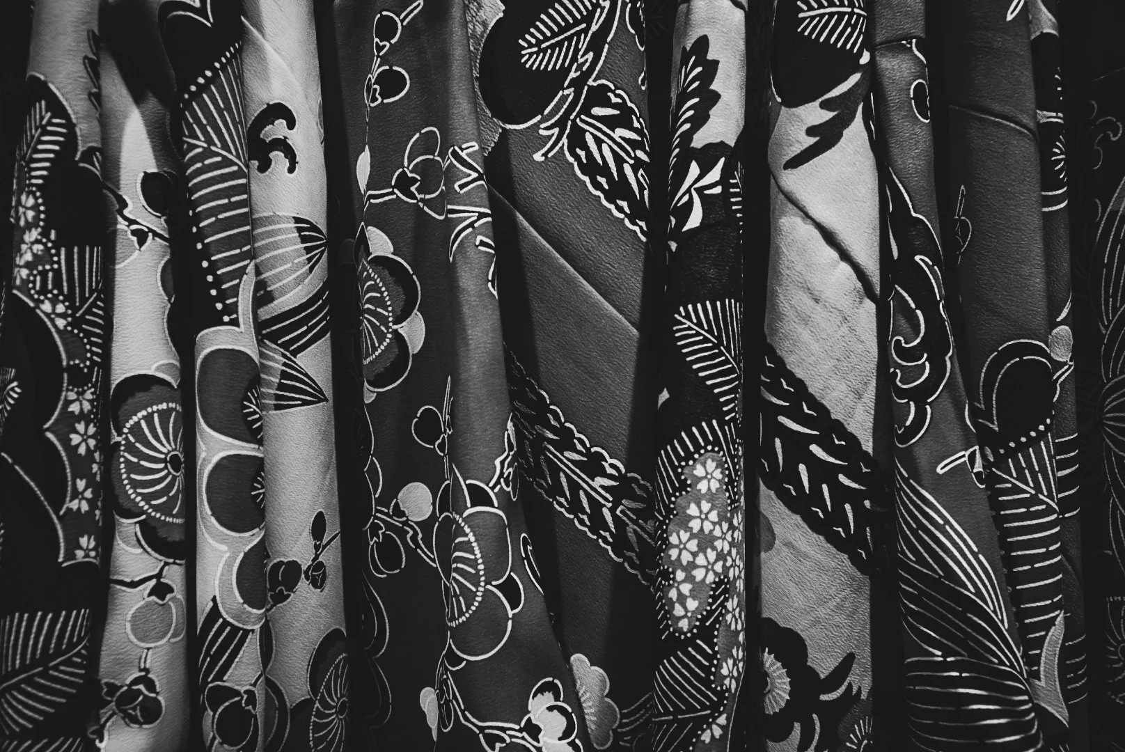 A collection of patterned fabric rolls, some with floral and leaf motifs, arranged vertically in black and white.