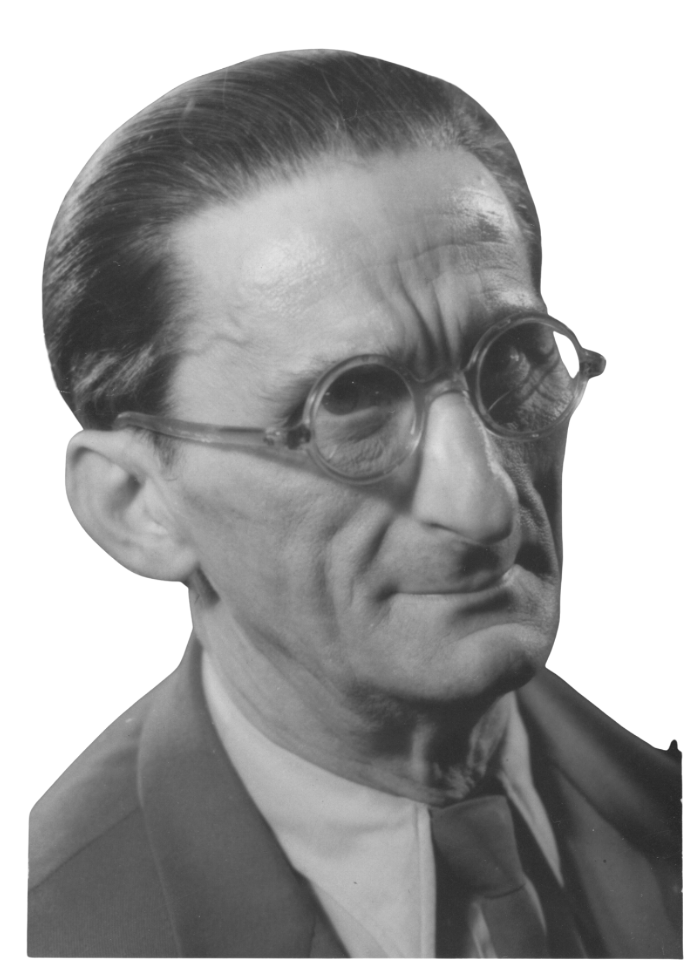 A black and white portrait of Julio Baghy, wearing round glasses, a tuxedo, and a bow tie, with a serious expression.