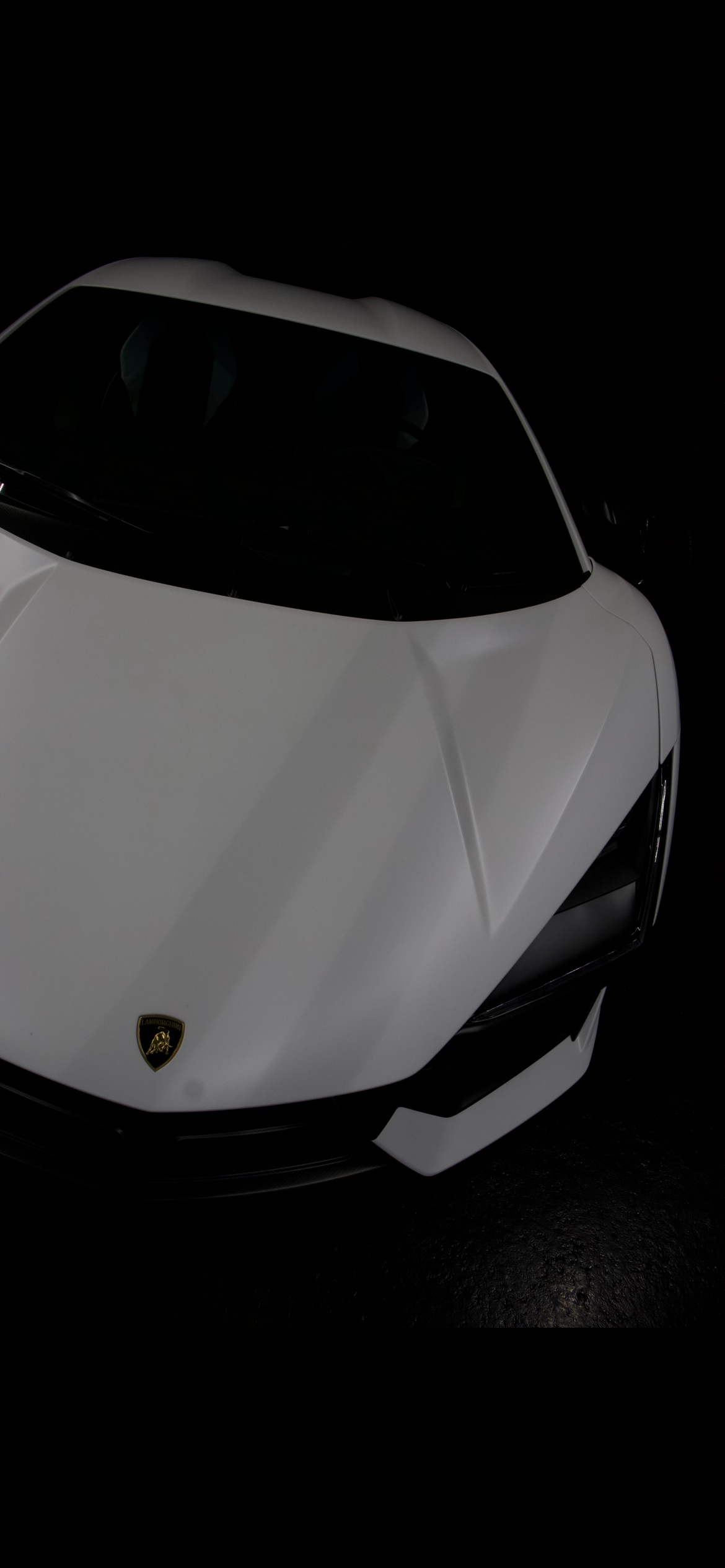 Front partial view of a white Lamborghini sports car with black accents, shown in low lighting.