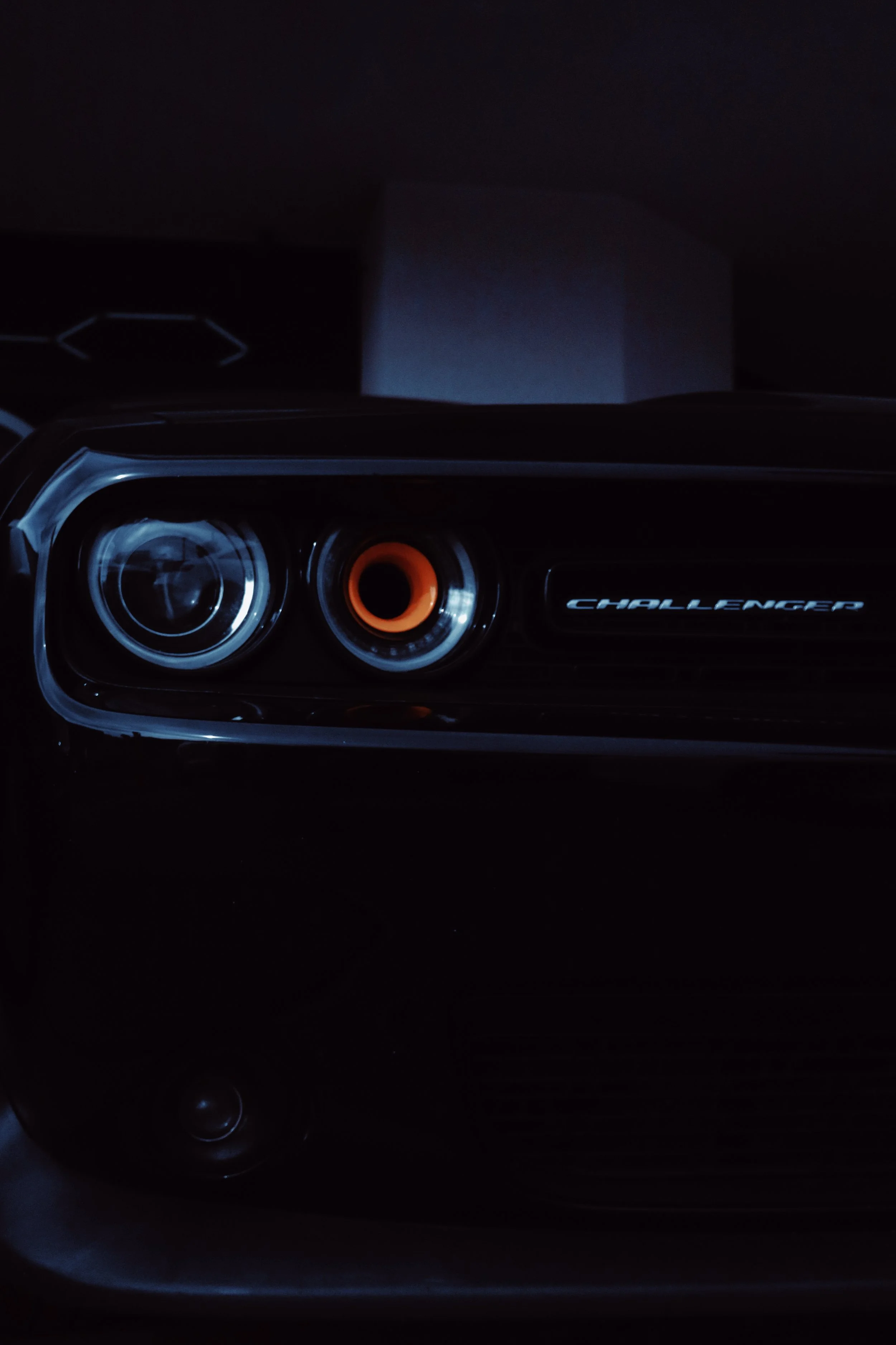 Close-up view of a vehicle's front headlight and the word 'CHALLENGER' on the car's front panel.