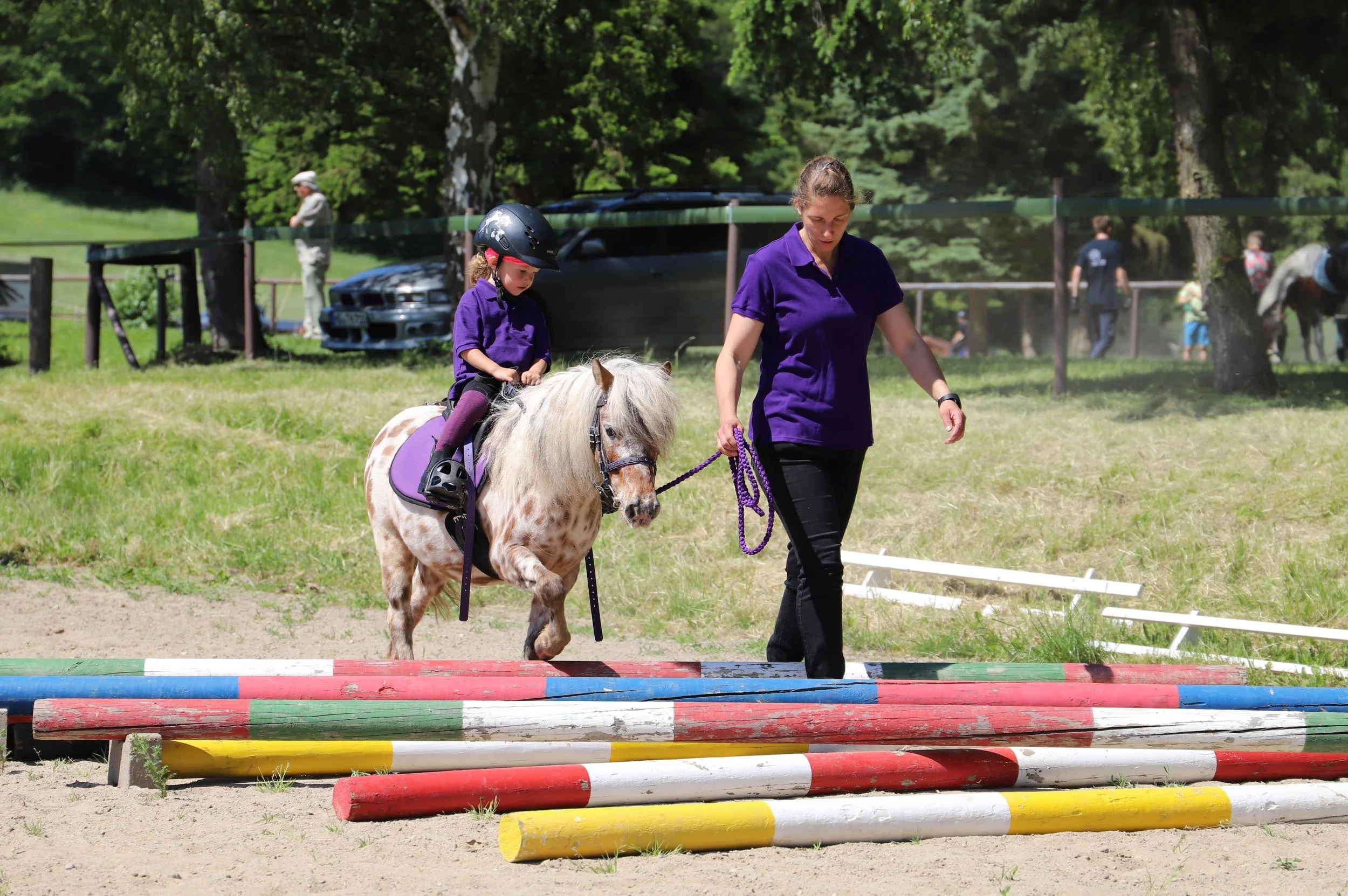 Mädchen wird auf Pony geführt und reitet über Stangen