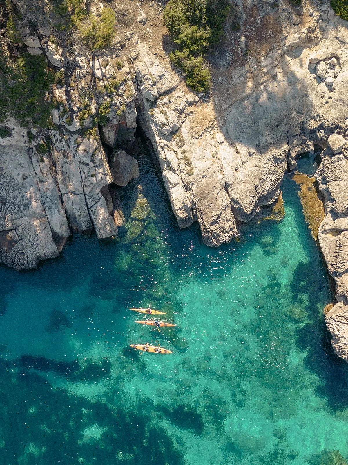 Vista cenital de varios kayaks sobre aguas transparentes de color turquesa, junto a la costa mediterránea de Menorca.