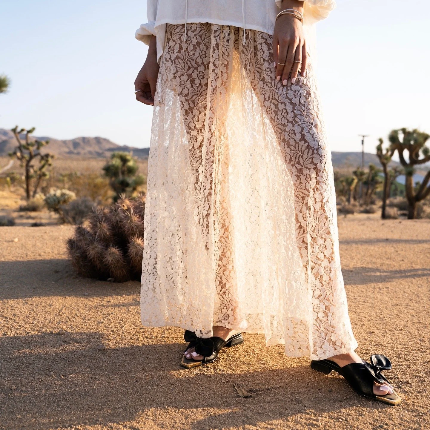BRÓG black embellished flat sandals worn with a cream lace dress, shot in the desert.