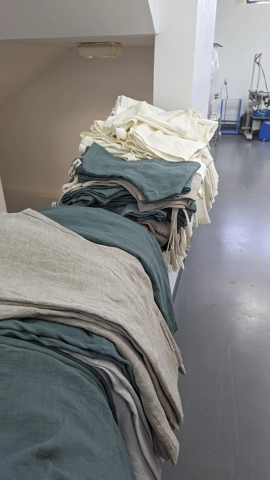 Folded fabric in muted sage, grey and oatmeal tones, stacked in the studio.