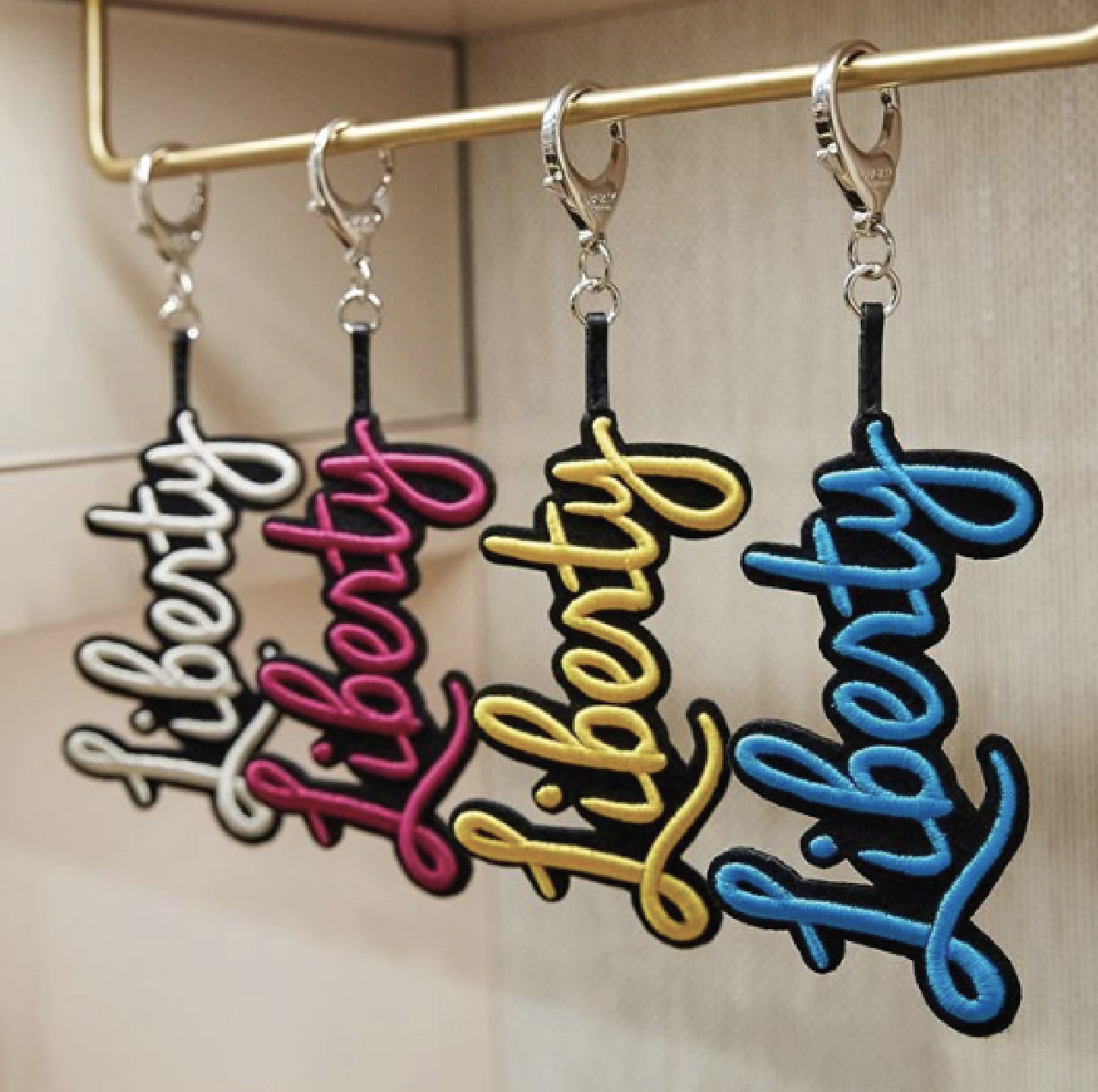 Row of embroidered script-word charms in different colours, hung on a rail