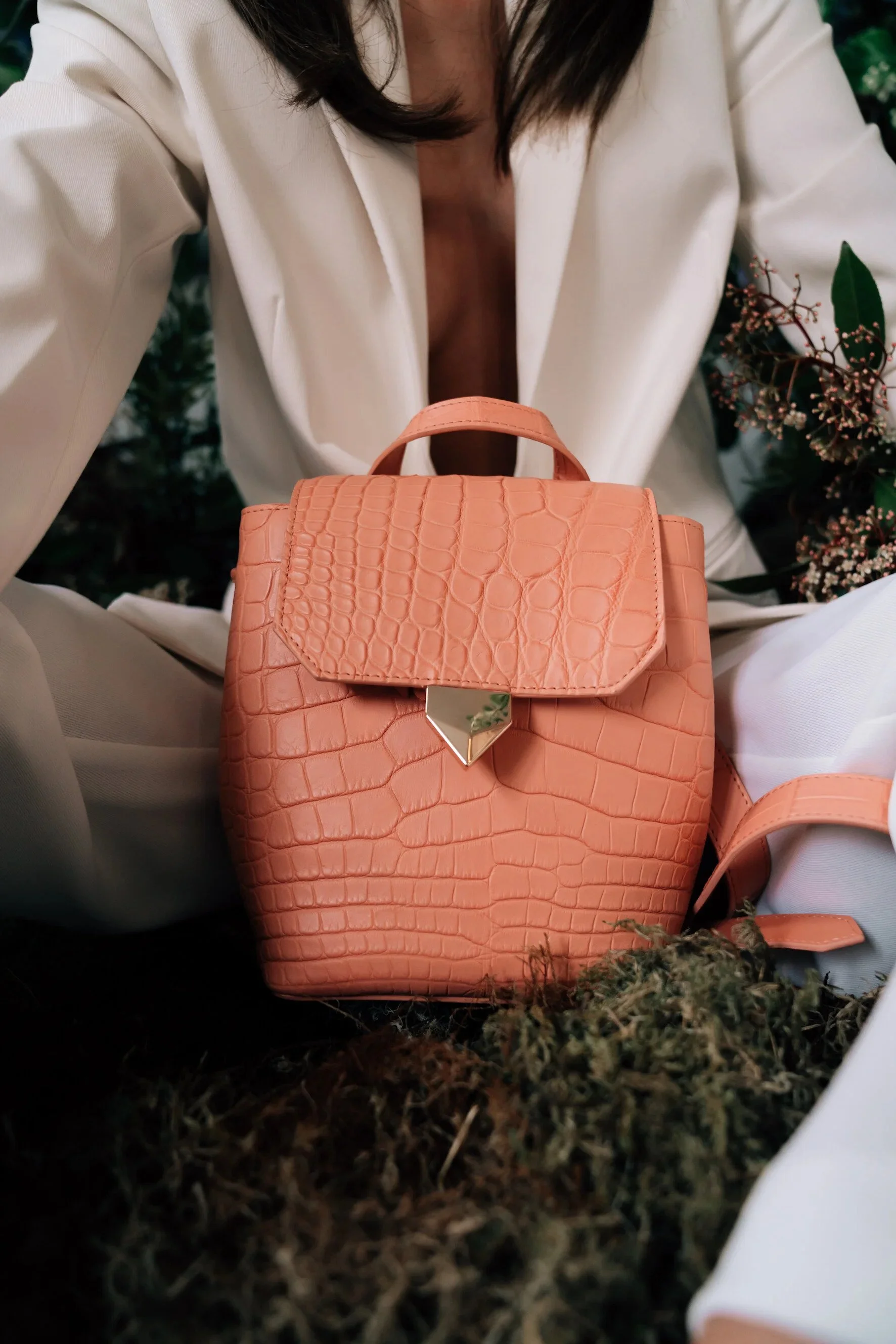 Shwaz terracotta crocodile-leather backpack with gold hardware, held by a model in a cream blazer.
