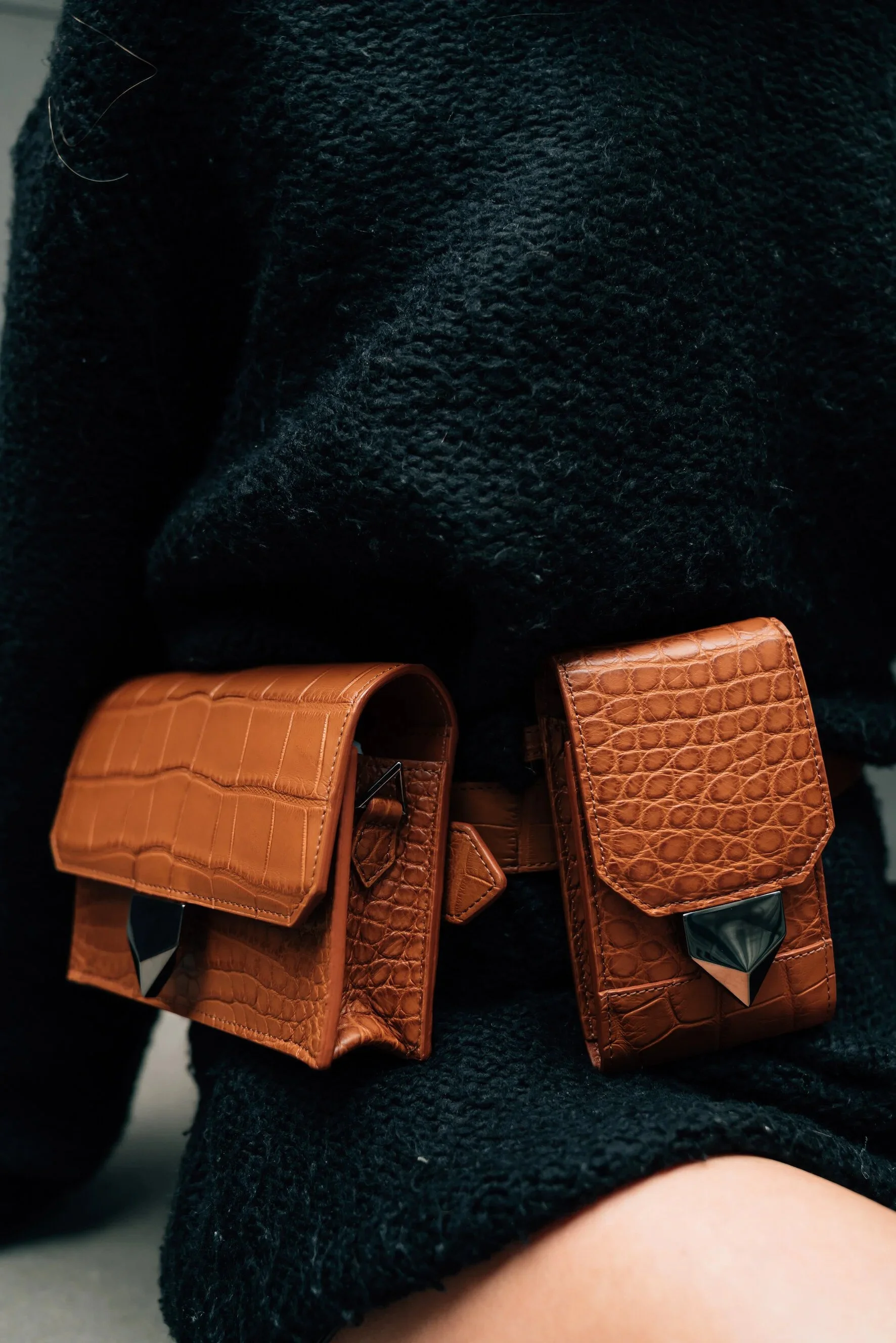 Shwaz tan crocodile-leather belt bags with gold hardware, worn over dark knitwear.