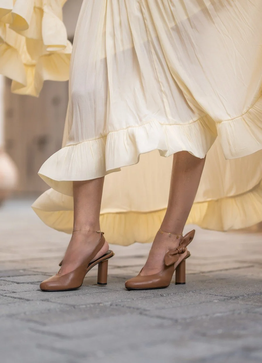 BRÓG tan leather slingback block-heel sandals worn with a cream ruffled dress.
