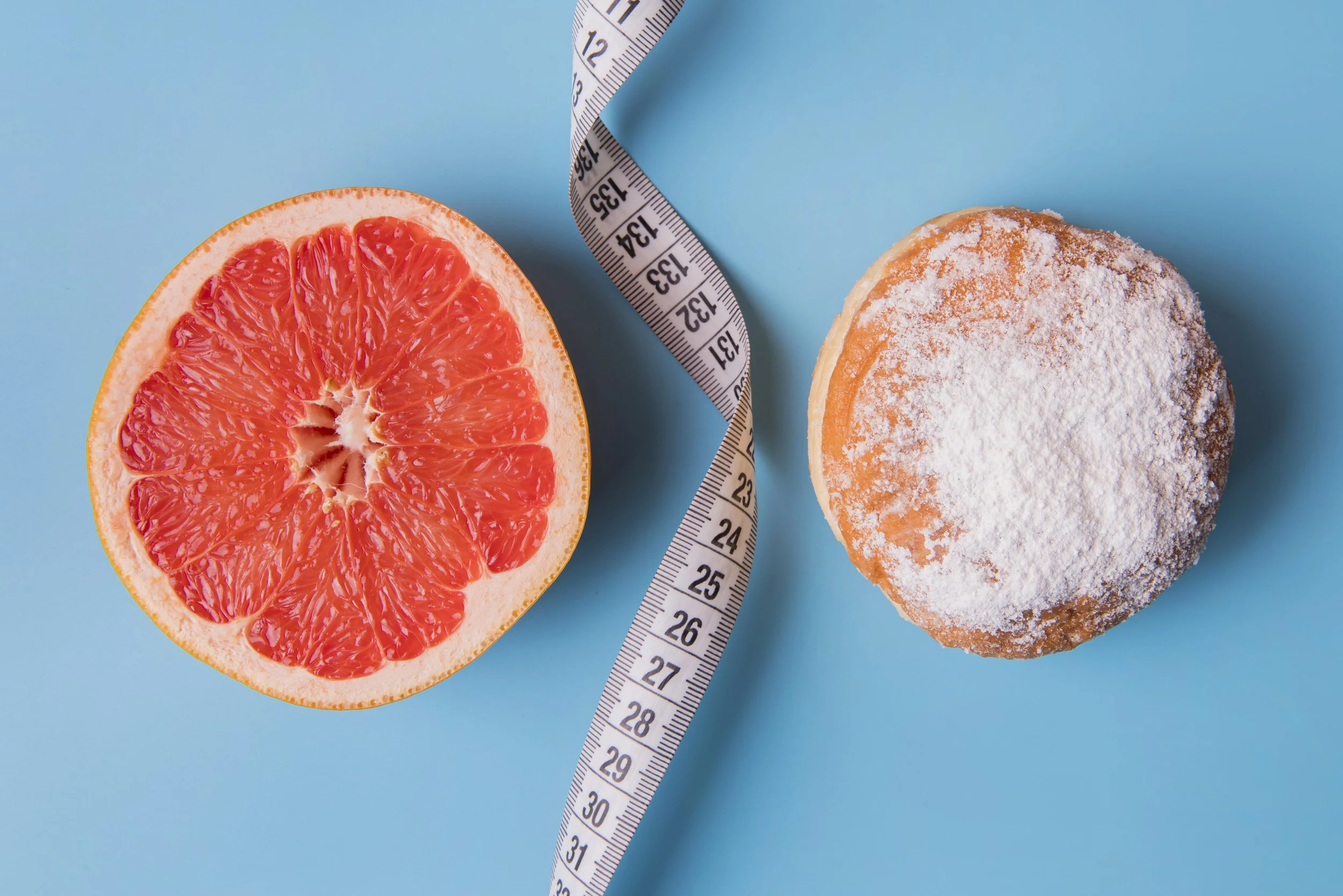 Halbierte Grapefruit, Meßband und ein mit Puderzucker bedeckter Kuchen auf einem blauen Hintergrund.