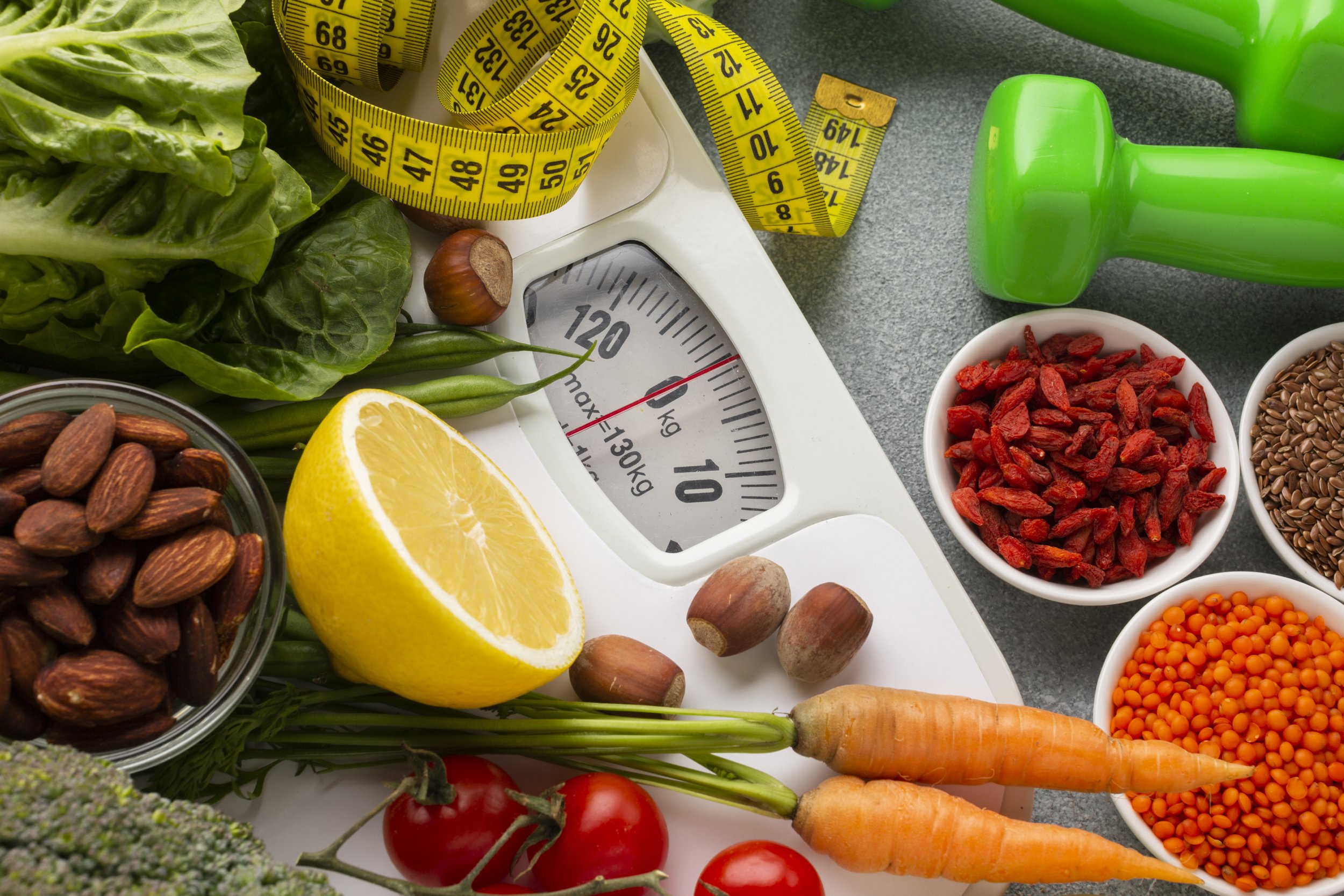 Gemüse, Nüsse, Samen, eine Küchenwaage, ein Messband, Hanteln und eine Zitrone, die anscheinend für eine gesunde Ernährung und Fitness verwendet werden.