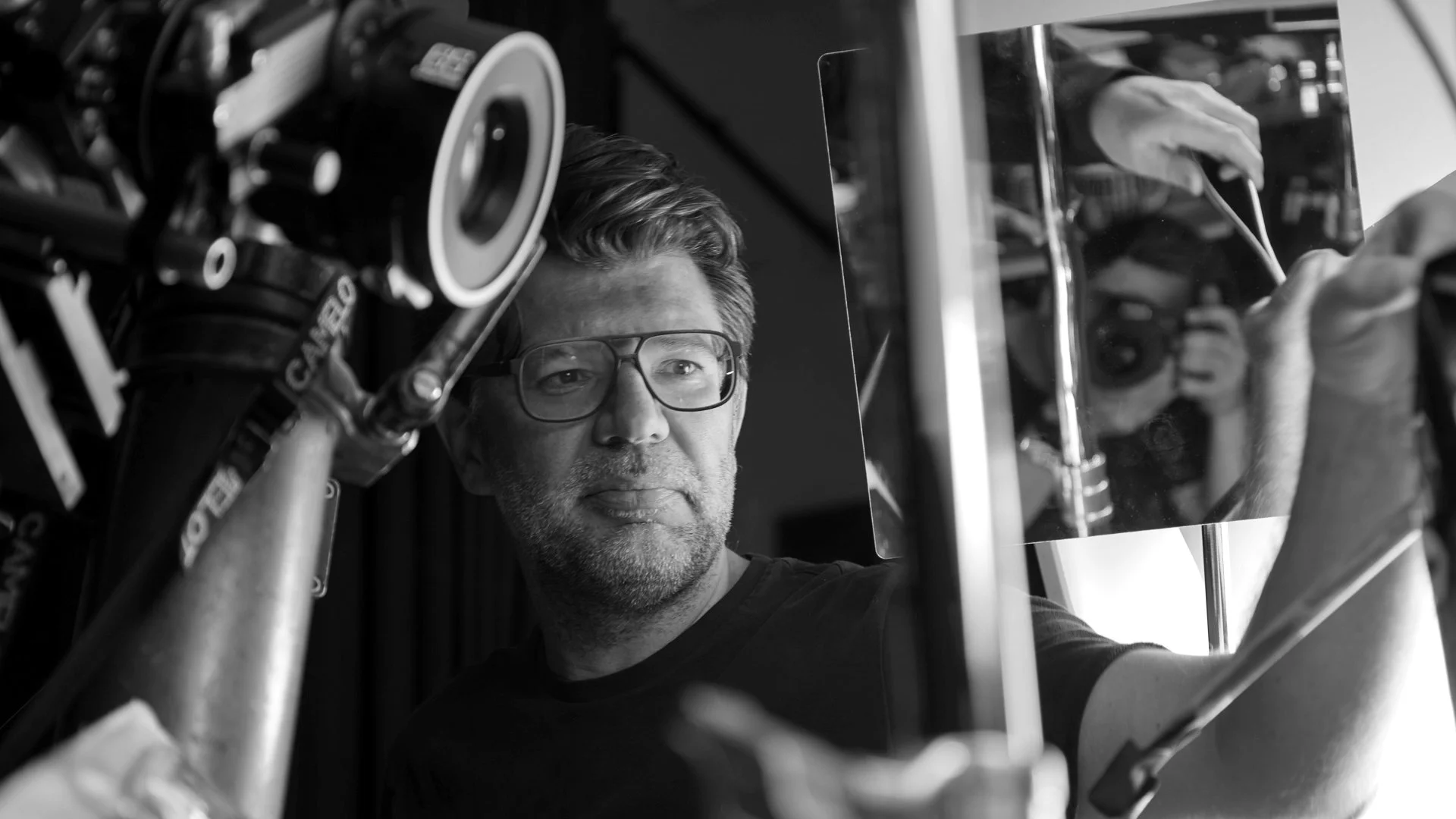 Ein Mann mit Brille betrachtet ein Bild, das eine Kamera zeigt, während er in einem Fotostudio arbeitet.