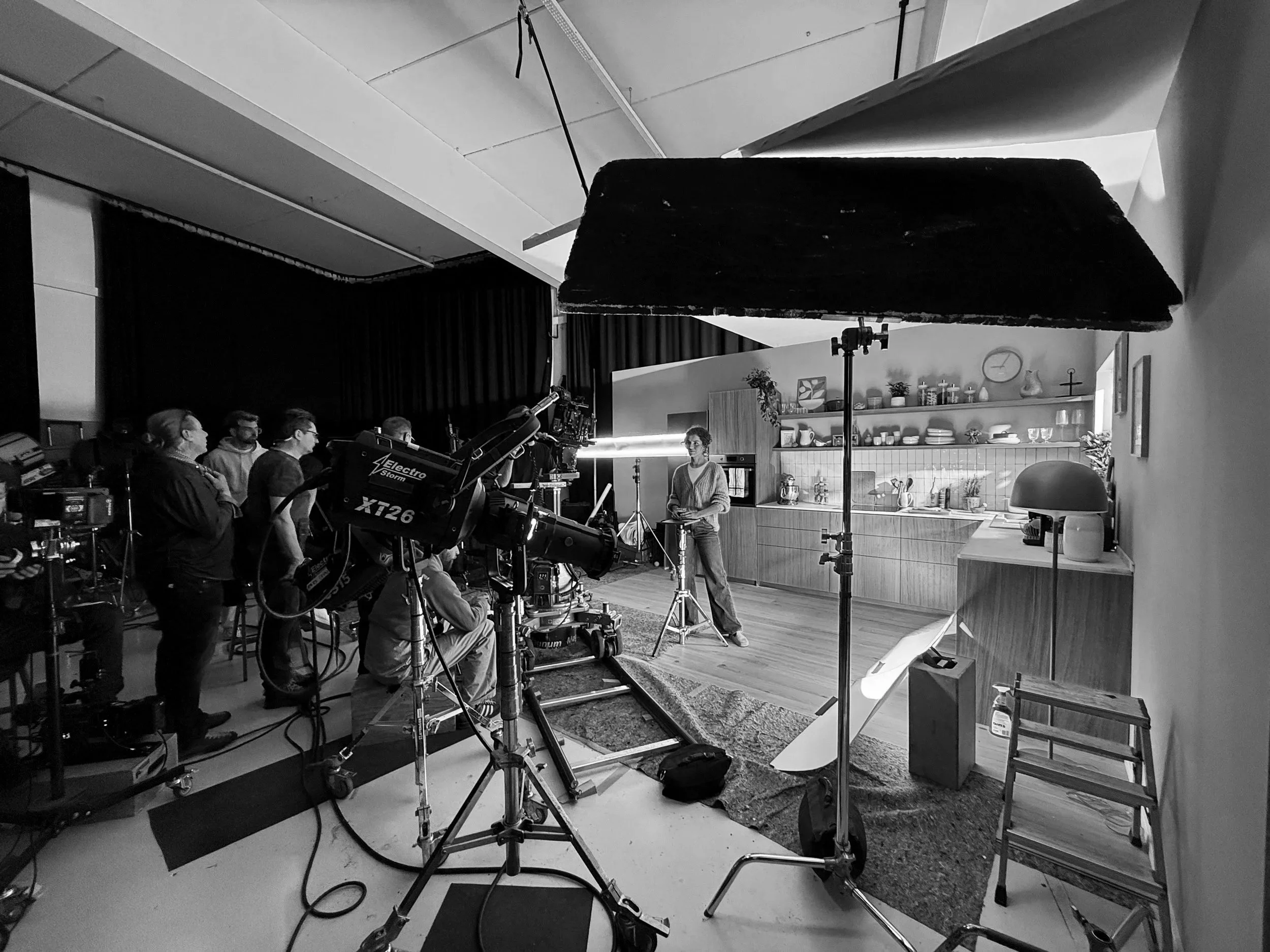 Ein Filmcrew dreht in einer modernen, gut eingerichteten Küche. Es gibt professionelle Kameras, Lichtausrüstung und mehrere Personen, die an der Produktion beteiligt sind.