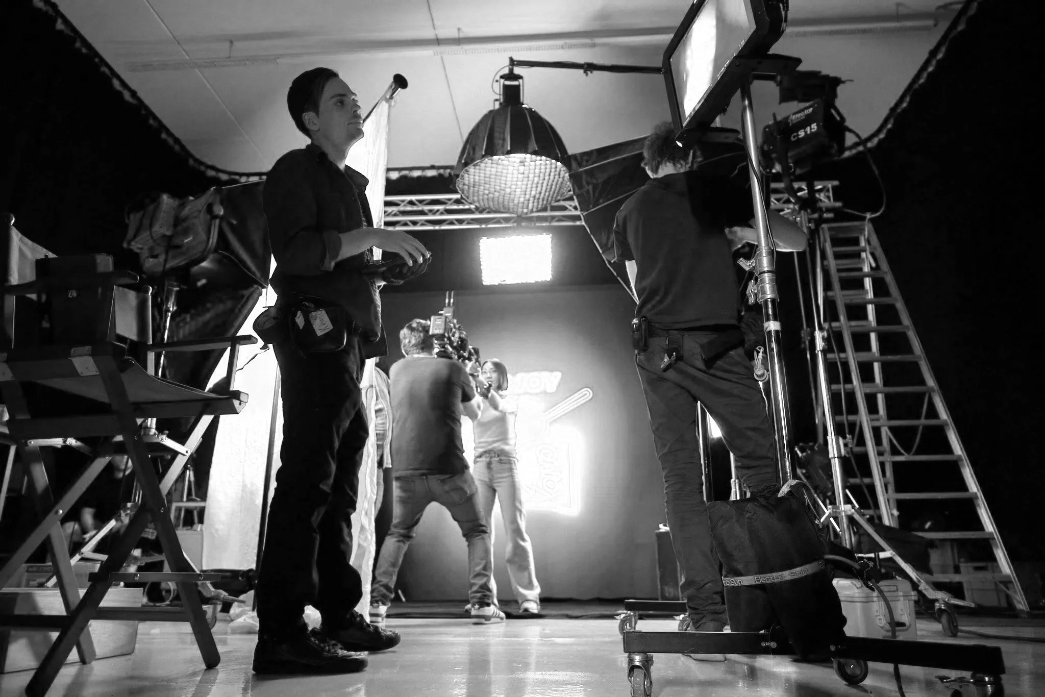 Drei Personen im Studio bei einem Video-Dreh, technisches Equipment und Beleuchtung sichtbar.