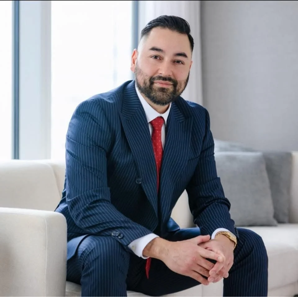 A man dressed in a suit and tie sits comfortably on a couch, exuding professionalism and poise