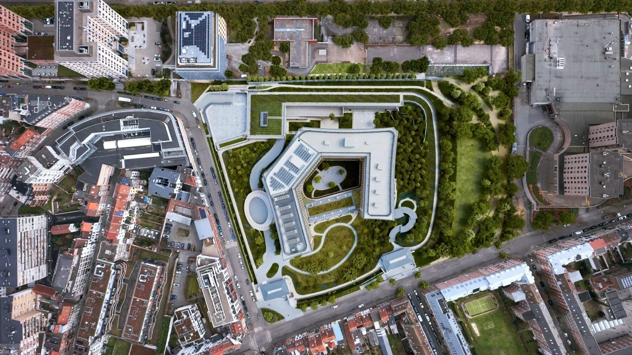 Vue aérienne d'un grand centre commercial moderne entouré d'arbres et de routes, avec plusieurs bâtiments et un parking.