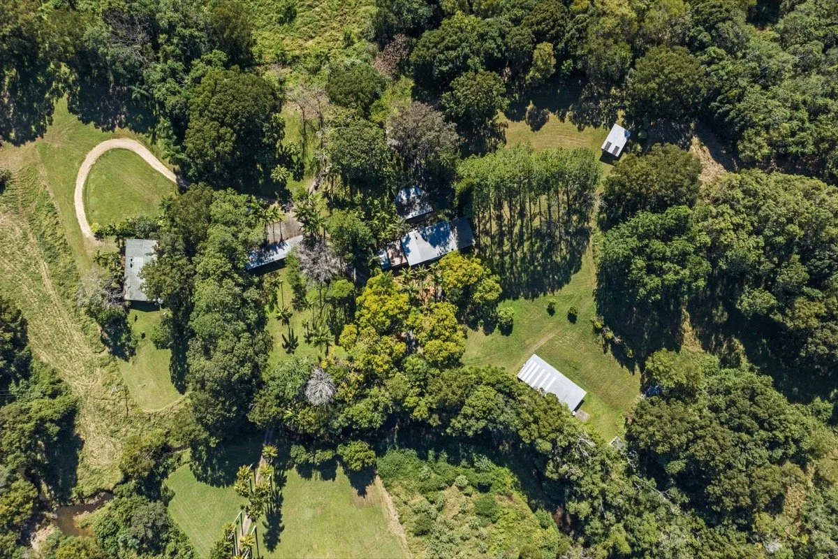 Aerial view of a green landscape with trees, grass fields, pathways, and several buildings.