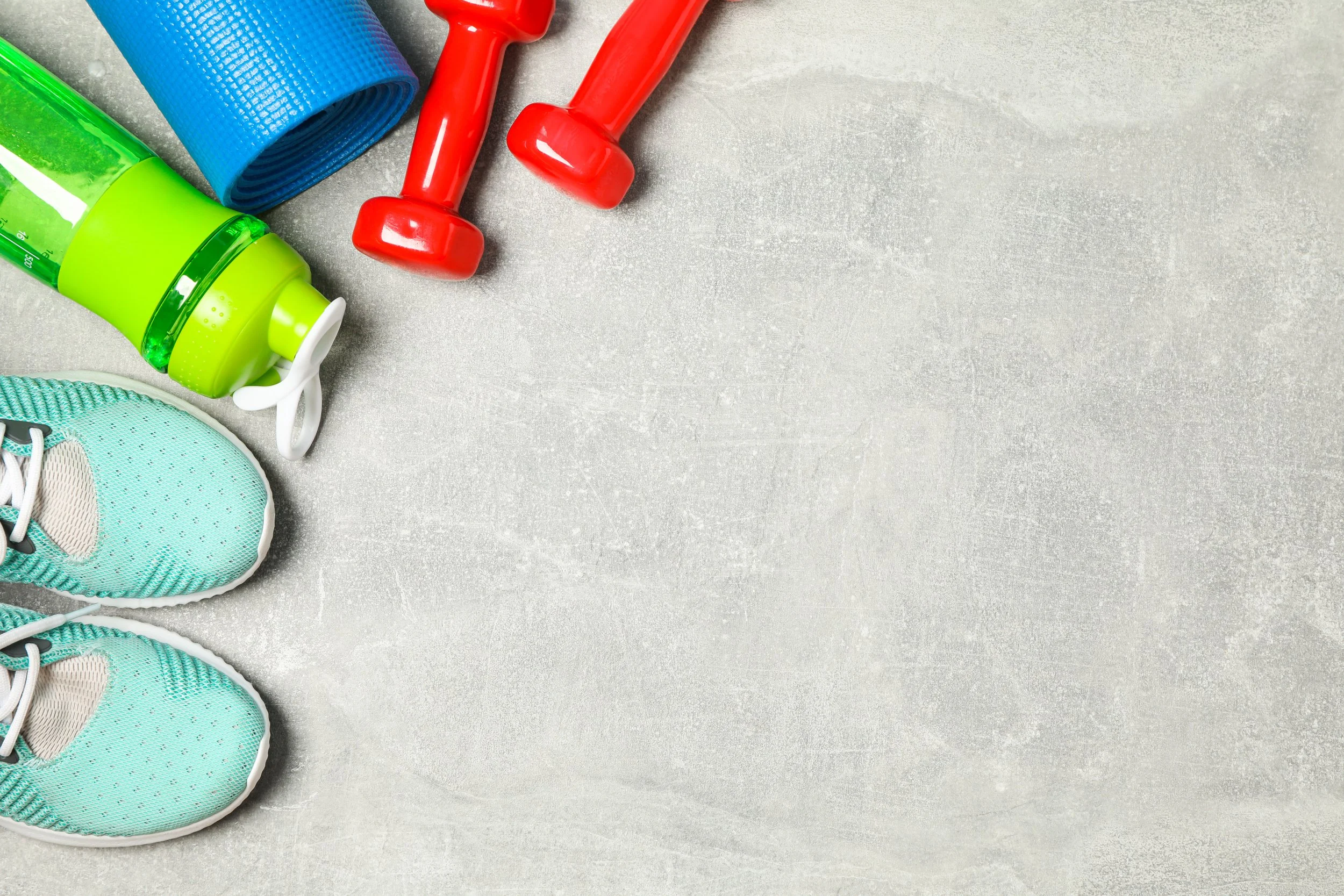 A pair of teal running shoes with white soles, a green water bottle, a blue yoga mat, and two red dumbbells on a gray textured surface.