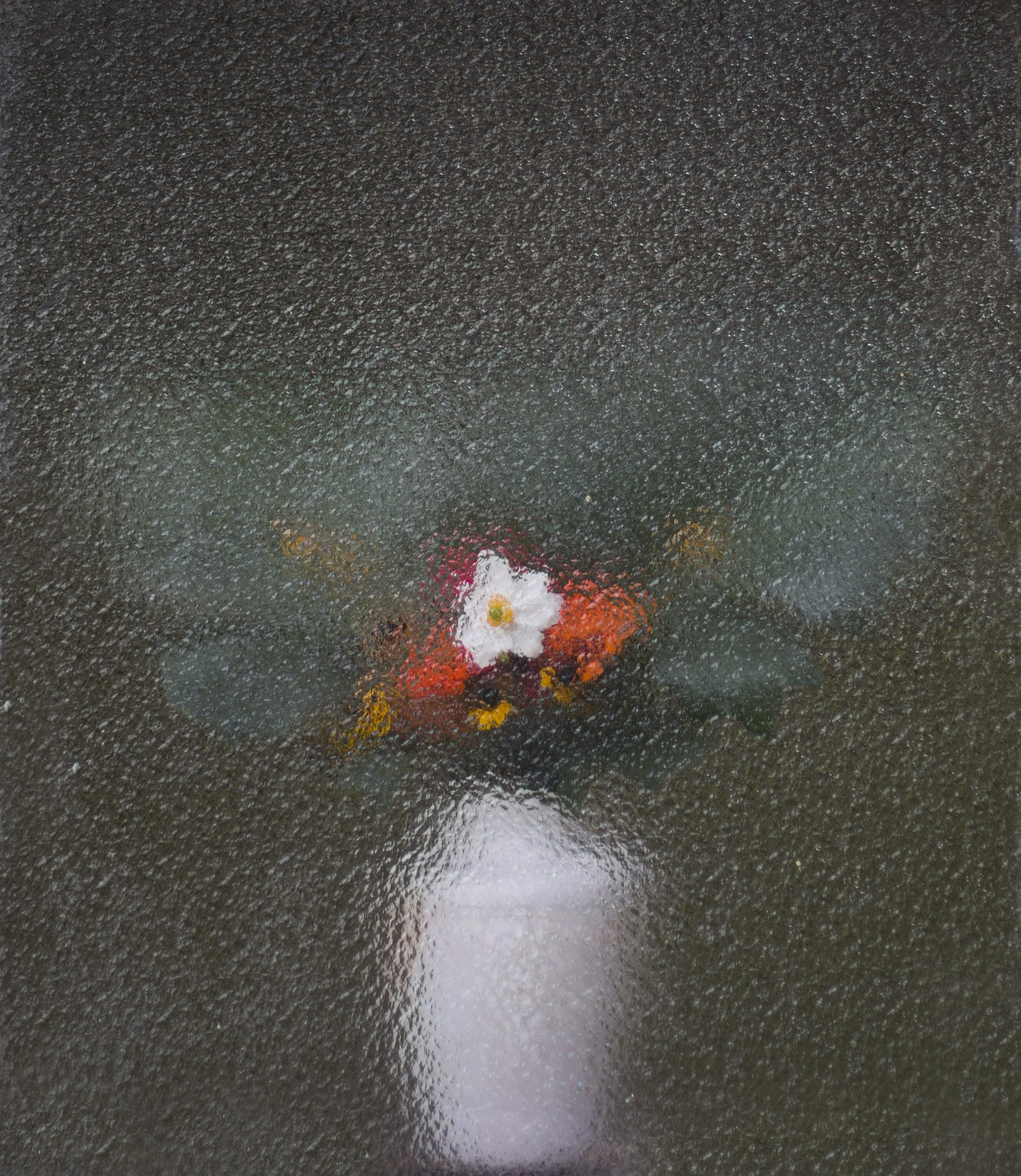 Close-up of a wet, textured asphalt surface with reflections and a small bouquet of flowers at the bottom center.