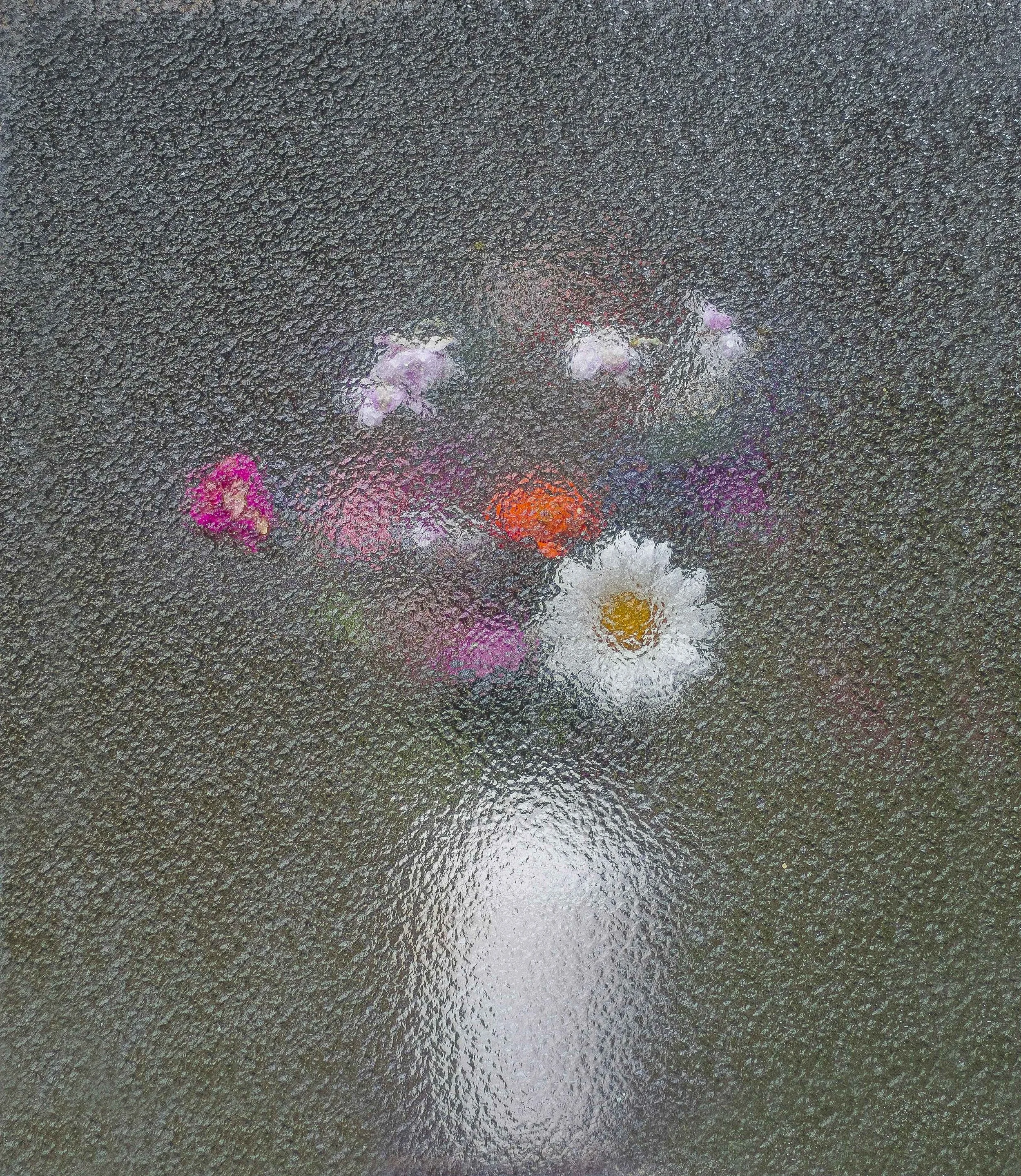 Reflected colorful flowers on a wet pavement with a textured surface.