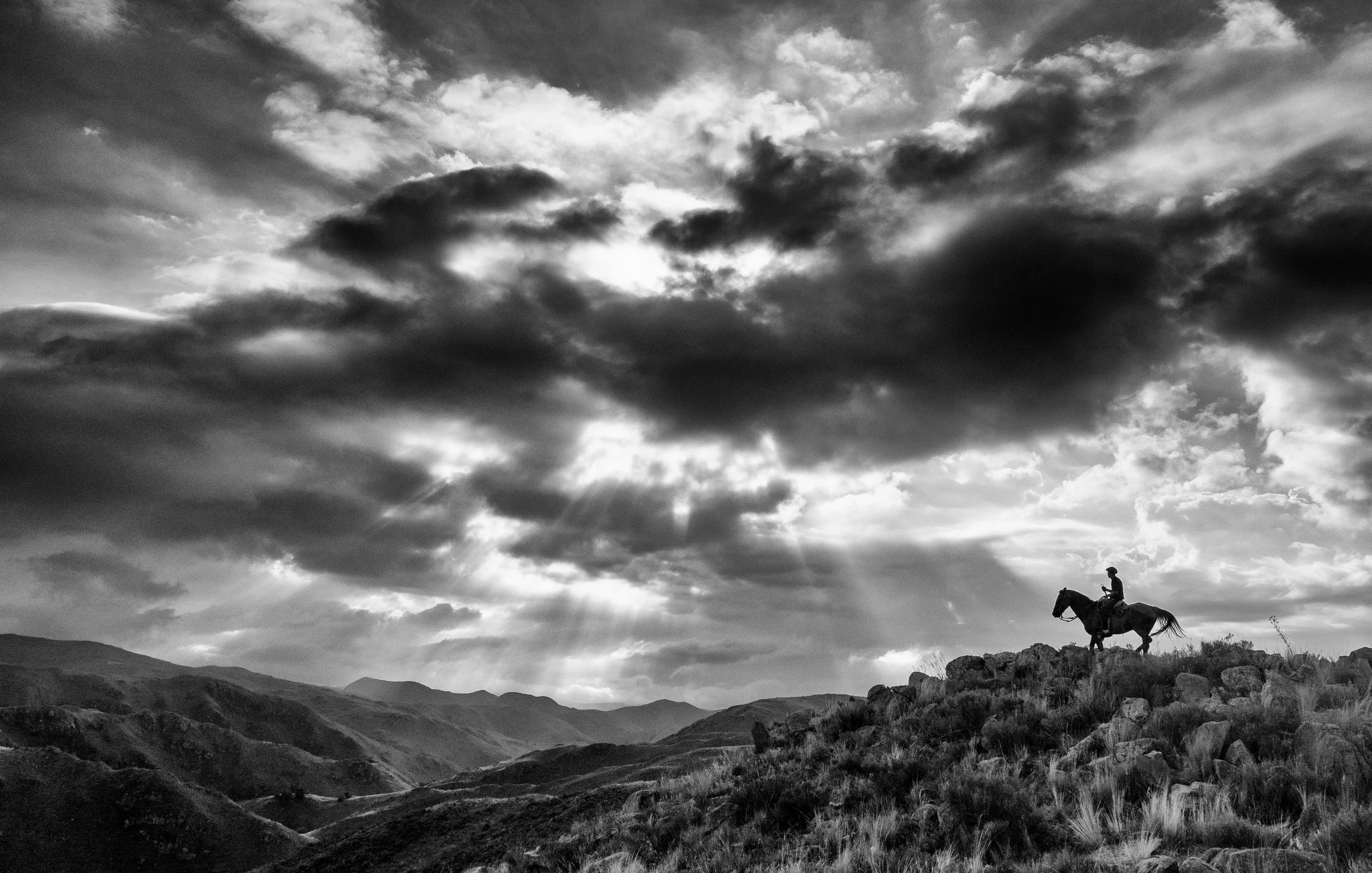 A person riding a horse on a rocky hill against a cloudy sky.