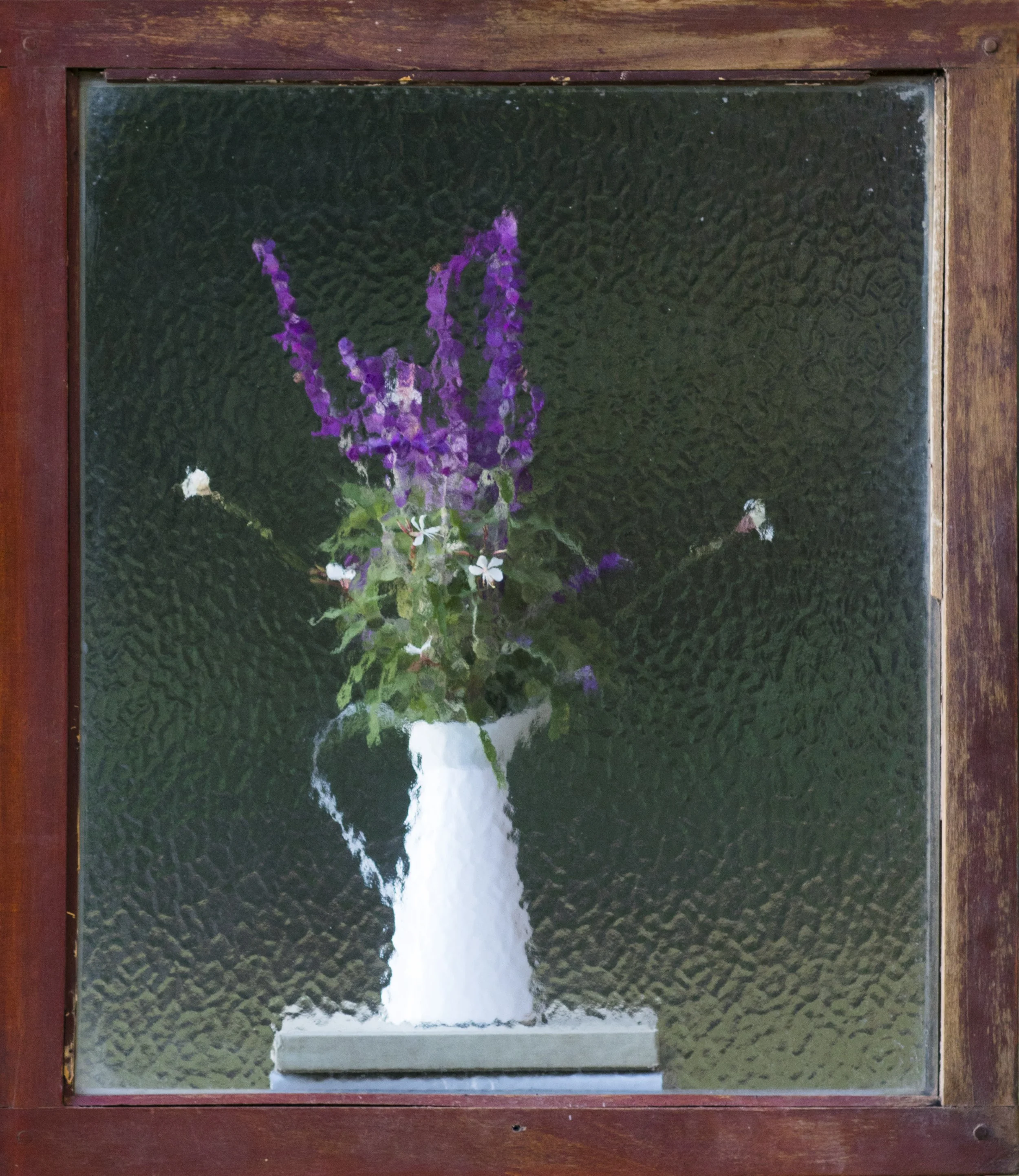 A potted plant with purple flowers and green leaves is reflected in a textured glass window set in a wooden frame.