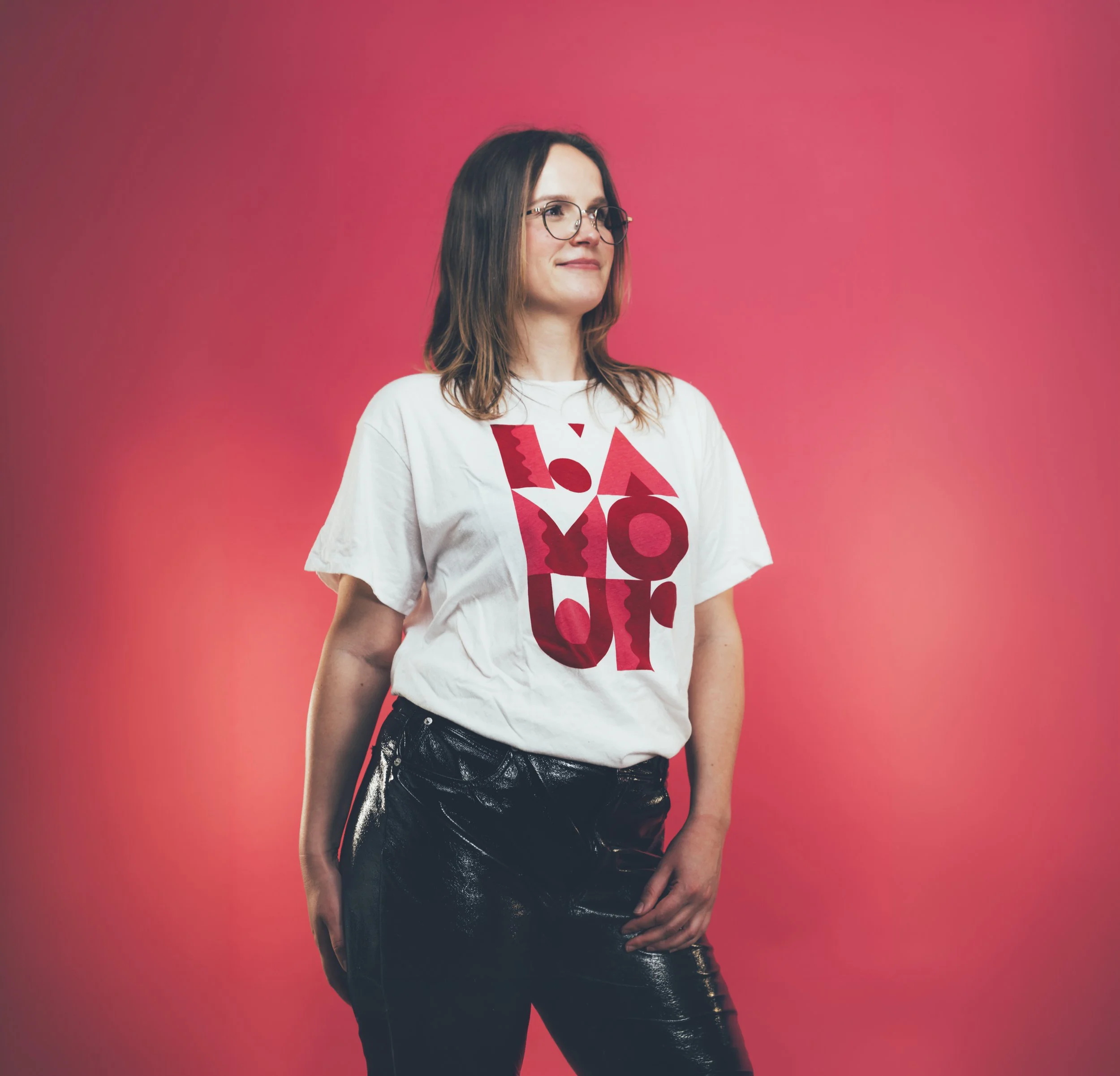 Léa Fanjat, présidente de l'association Keyframers Collective. Jeune femme avec lunettes, portant un t-shirt blanc avec écriture rouge, en veste de cuir noire, debout devant un mur rose.