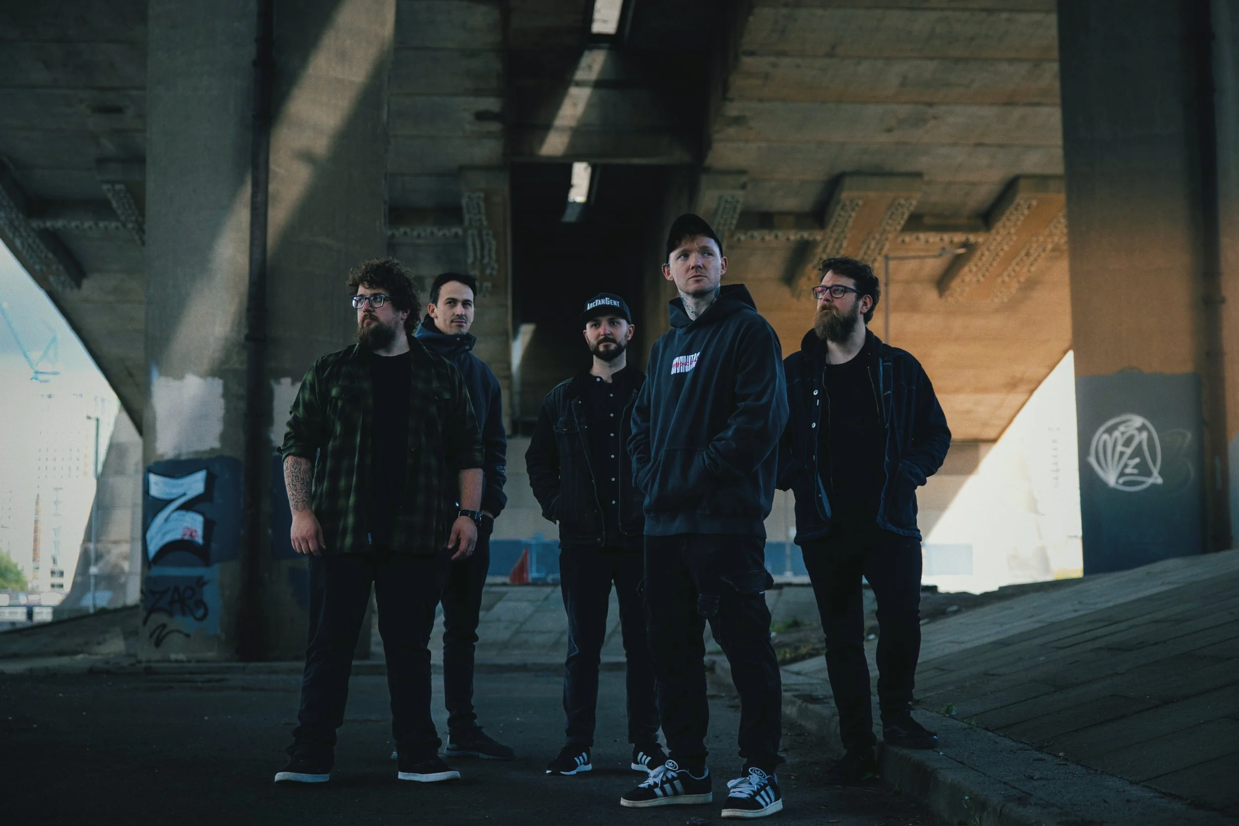Five members of Scottish Gaelic metalcore band Gun Ghaol standing beneath a concrete road bridge.
