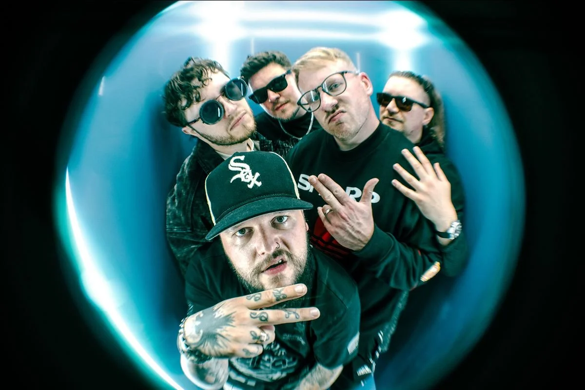 Five band members pose together in a blue-lit circular space.