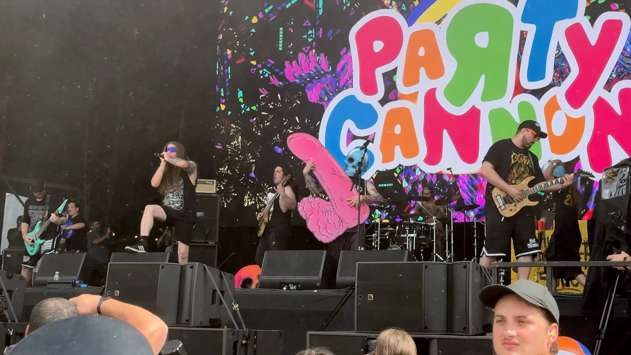 Party Cannon performing at Bloodstock 2026, with their colourful logo behind the band and a giant pink penis-shaped prop centre stage.