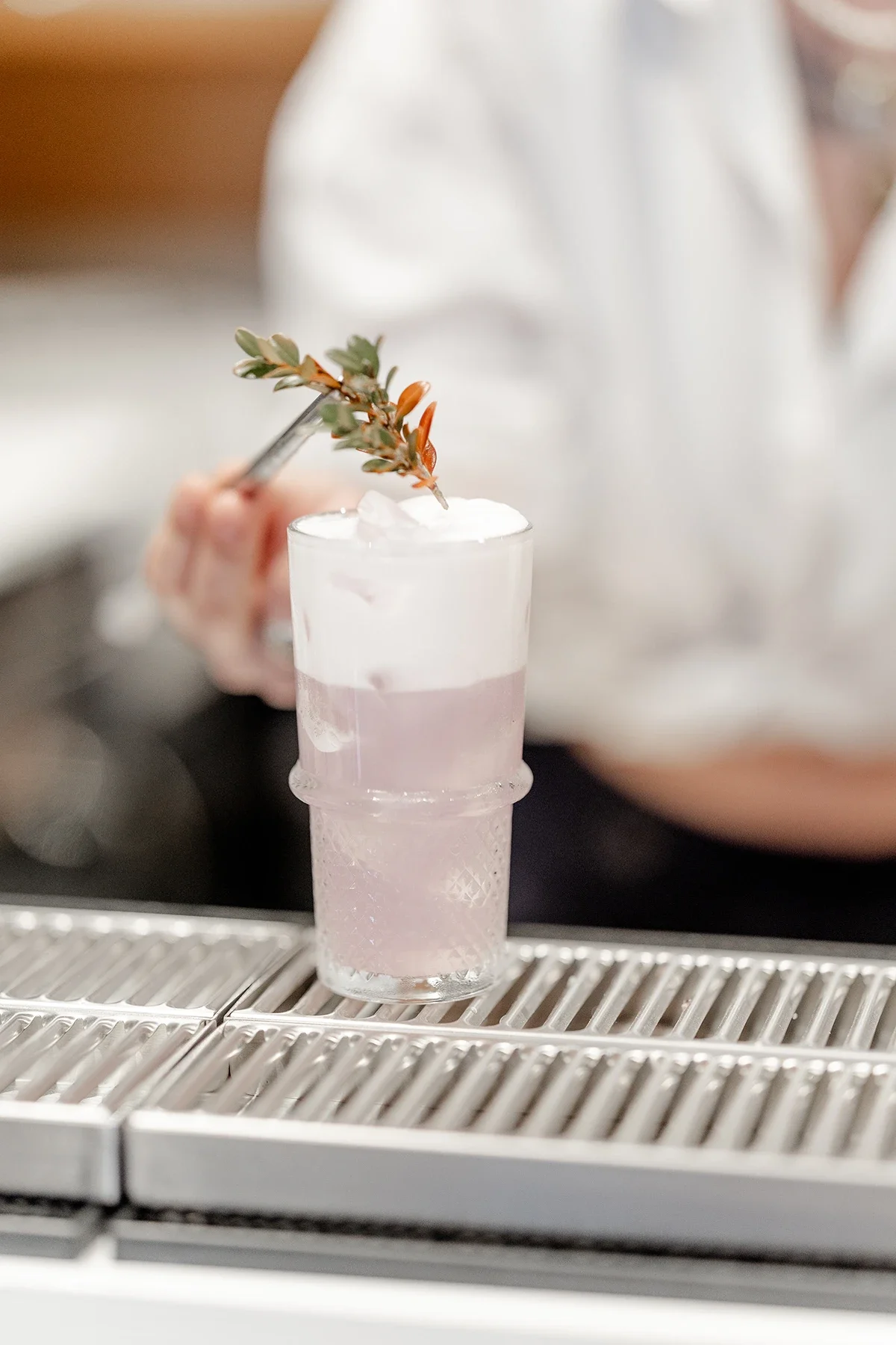 Personne préparant un cocktail dans un verre à cocktail avec une branche d'herbes