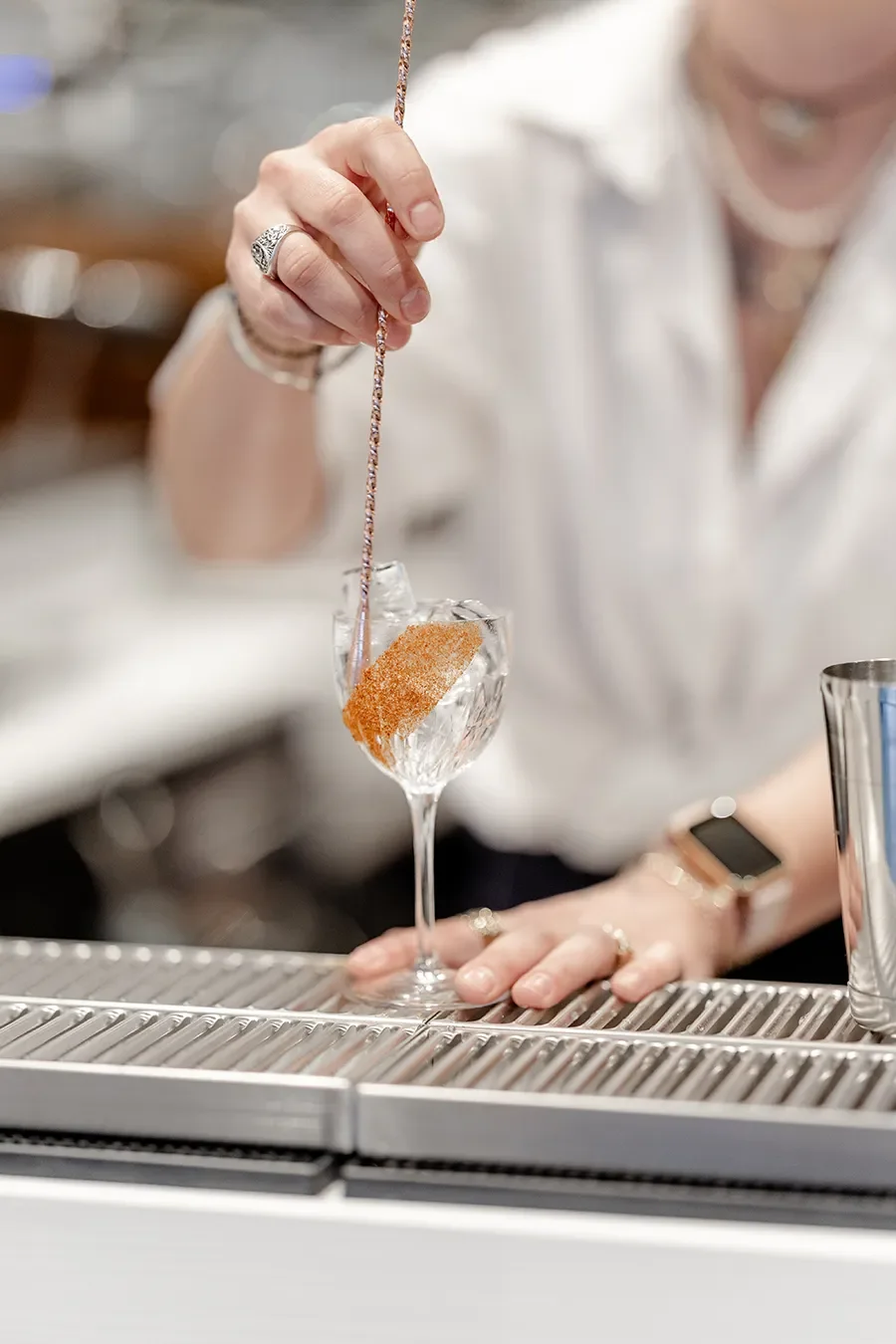 Une femme utilise une cuillère pour déposer un ingrédient ou un sirop dans un verre à cocktail en cristal avec de la glace.