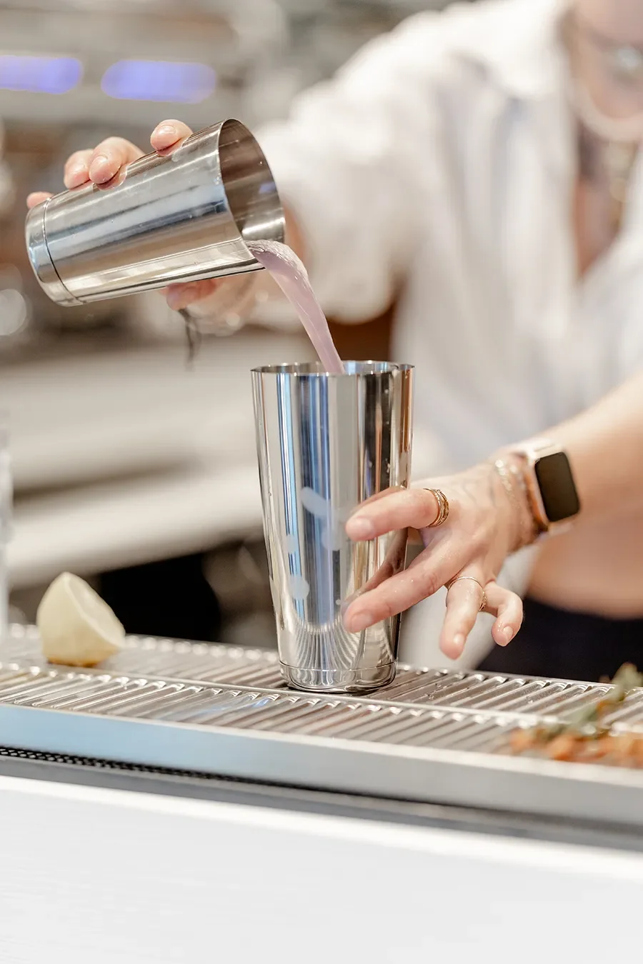 Une personne verse un liquide rose dans un verre métallique dans un bar ou un restaurant.