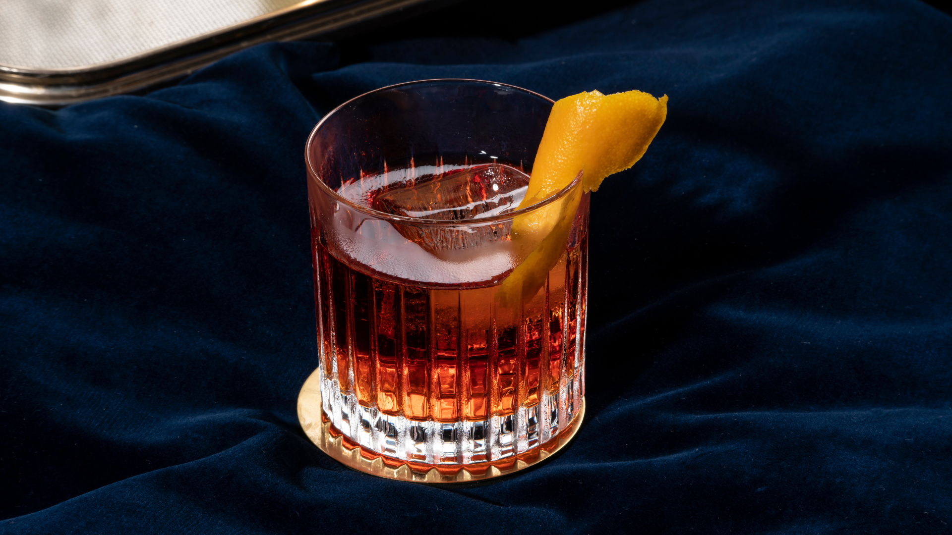 Verre de cocktail rouge avec tranche de citron, glace et décoration en fond noir et tissu bleu foncé.