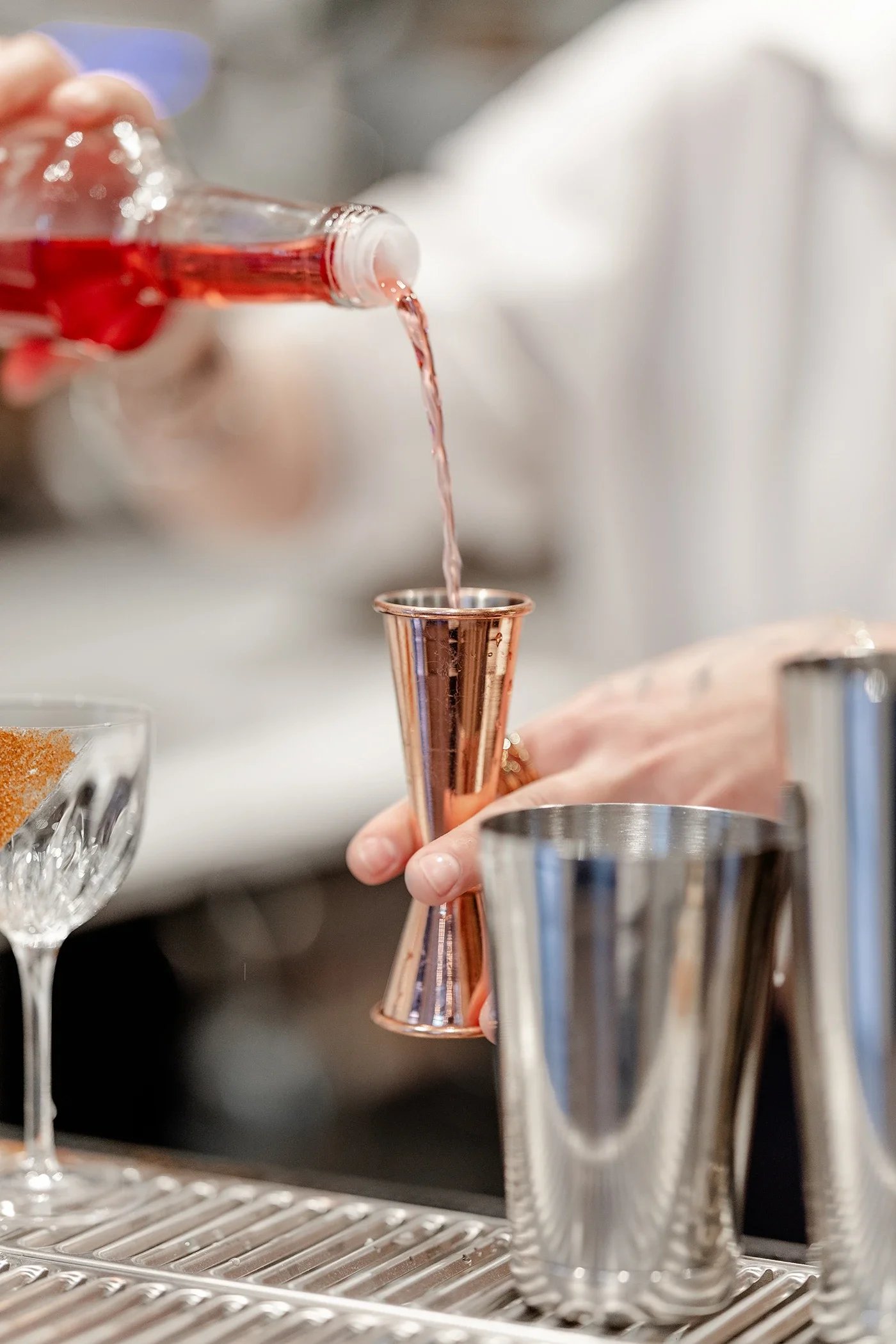 Une personne verse un liquide rosé dans un verre à cocktail en cuivre.