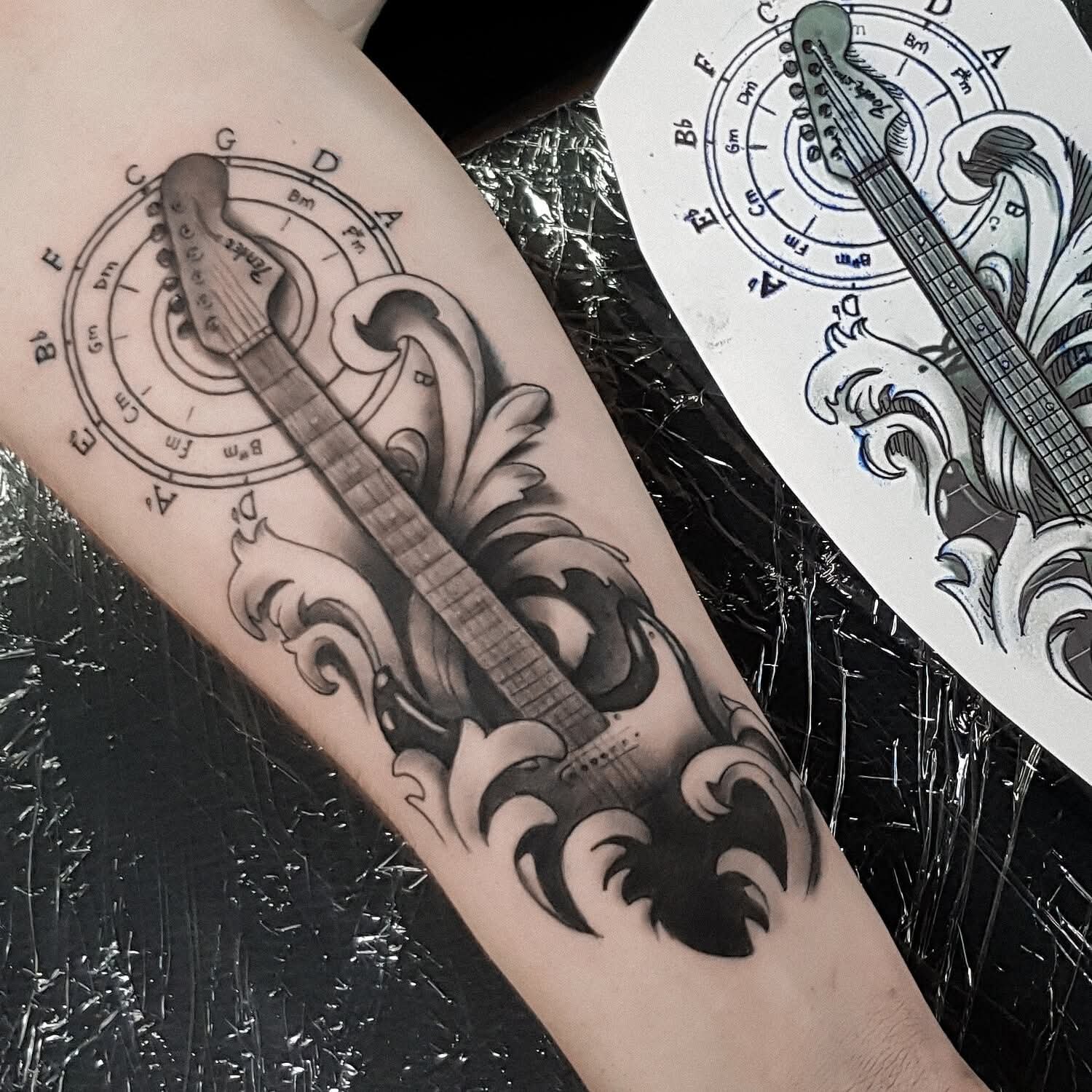 Tattoo eines gitarrens und kunstvollen Wellenmusters auf dem Unterarm, in Schwarz- und Grautönen, mit Notenlinien und musikalischen Noten im Hintergrund by Nika Nim tattoo Artist in Essen,Dusseldorf