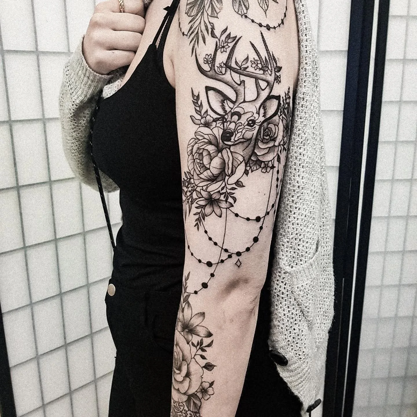 Schwarze Tattoo eines Hirsches mit Blumen und Perlen an einem Oberarm